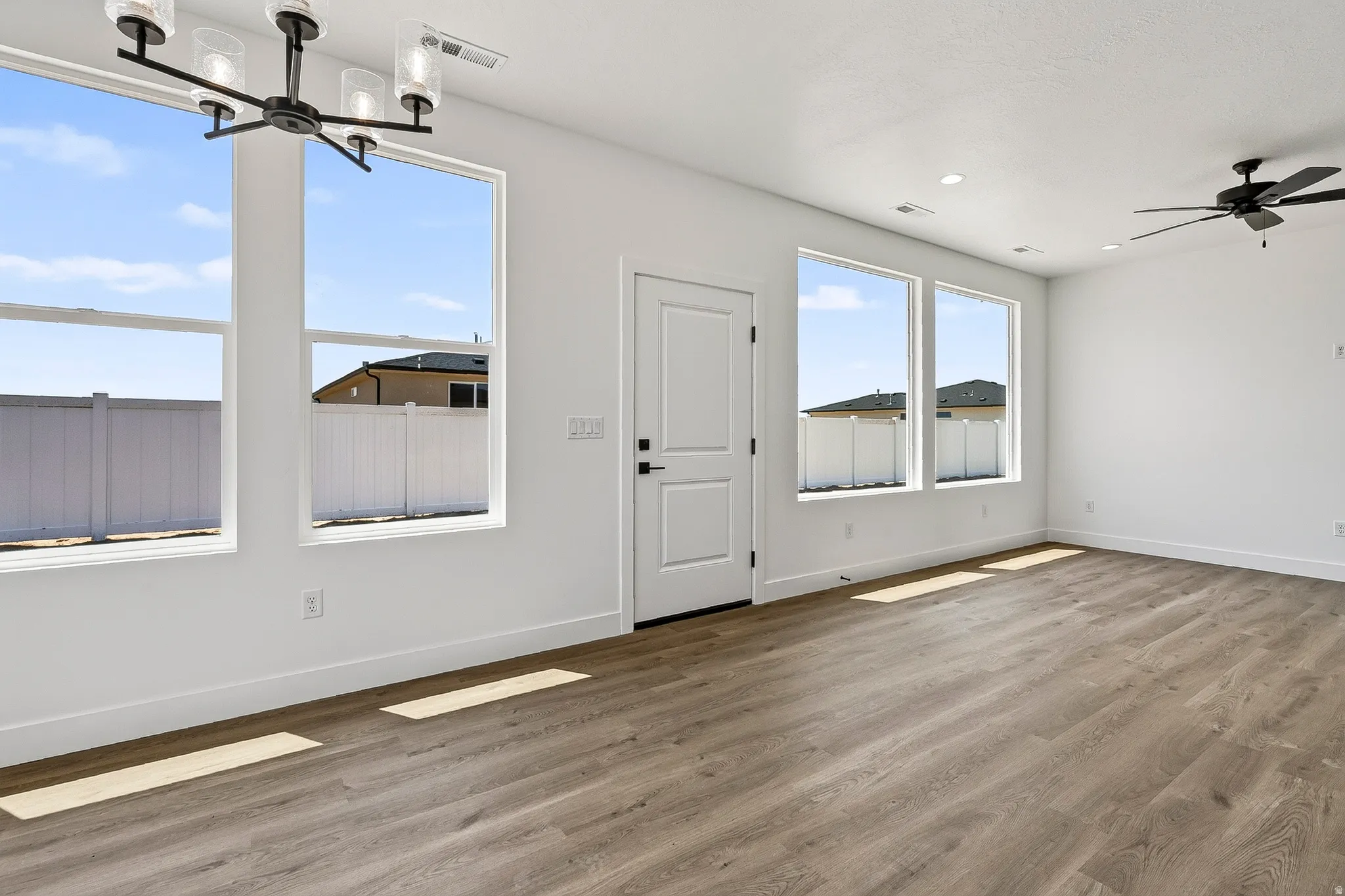 Spacious interior featuring wood-finish flooring, multiple large windows, a modern black chandelier, recessed lighting, and a ceiling fan