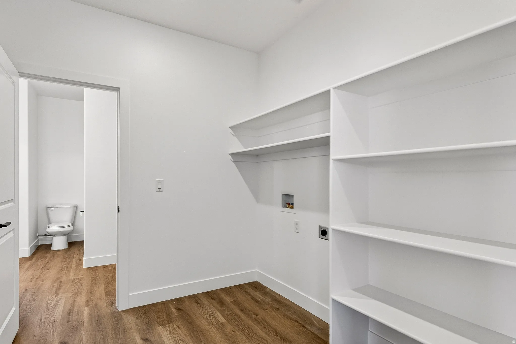 Utility space featuring extensive built-in shelving, wood-finish flooring, and white wall finishes