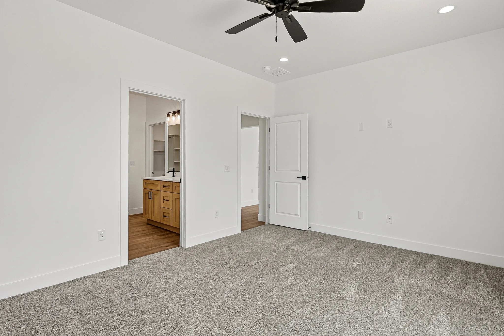 Spacious room featuring light gray carpeting and a black ceiling fan with recessed lighting