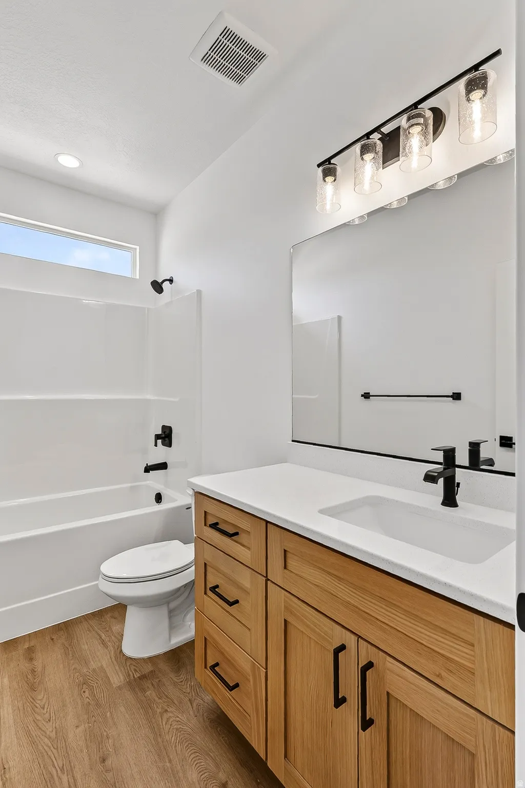 Bathroom featuring a light wood-finish vanity with black hardware, a white countertop with an integrated sink, and black fixtures