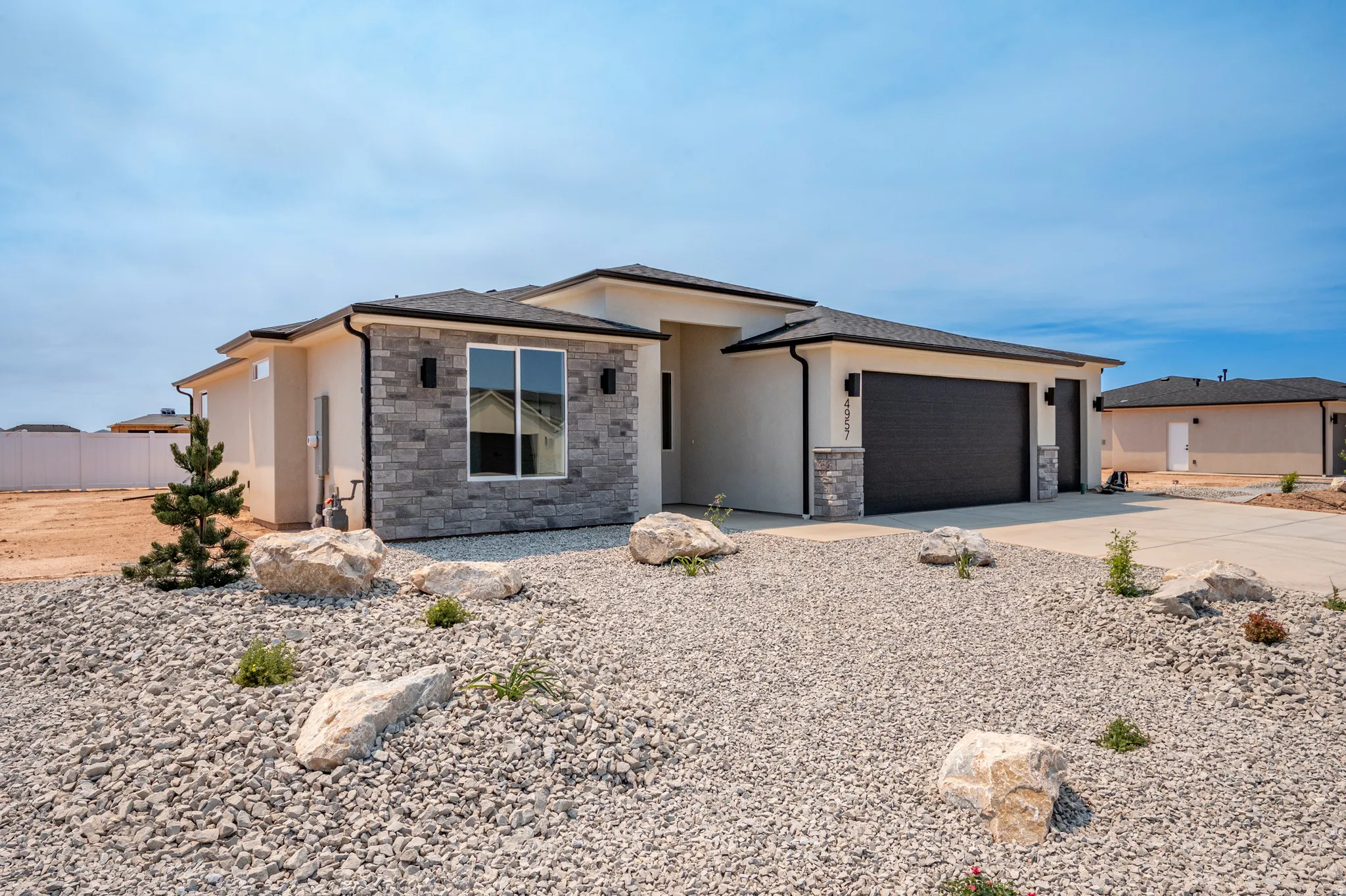 Contemporary stucco exterior with stacked stone accents, a dark garage door, and a gravel and boulder landscape