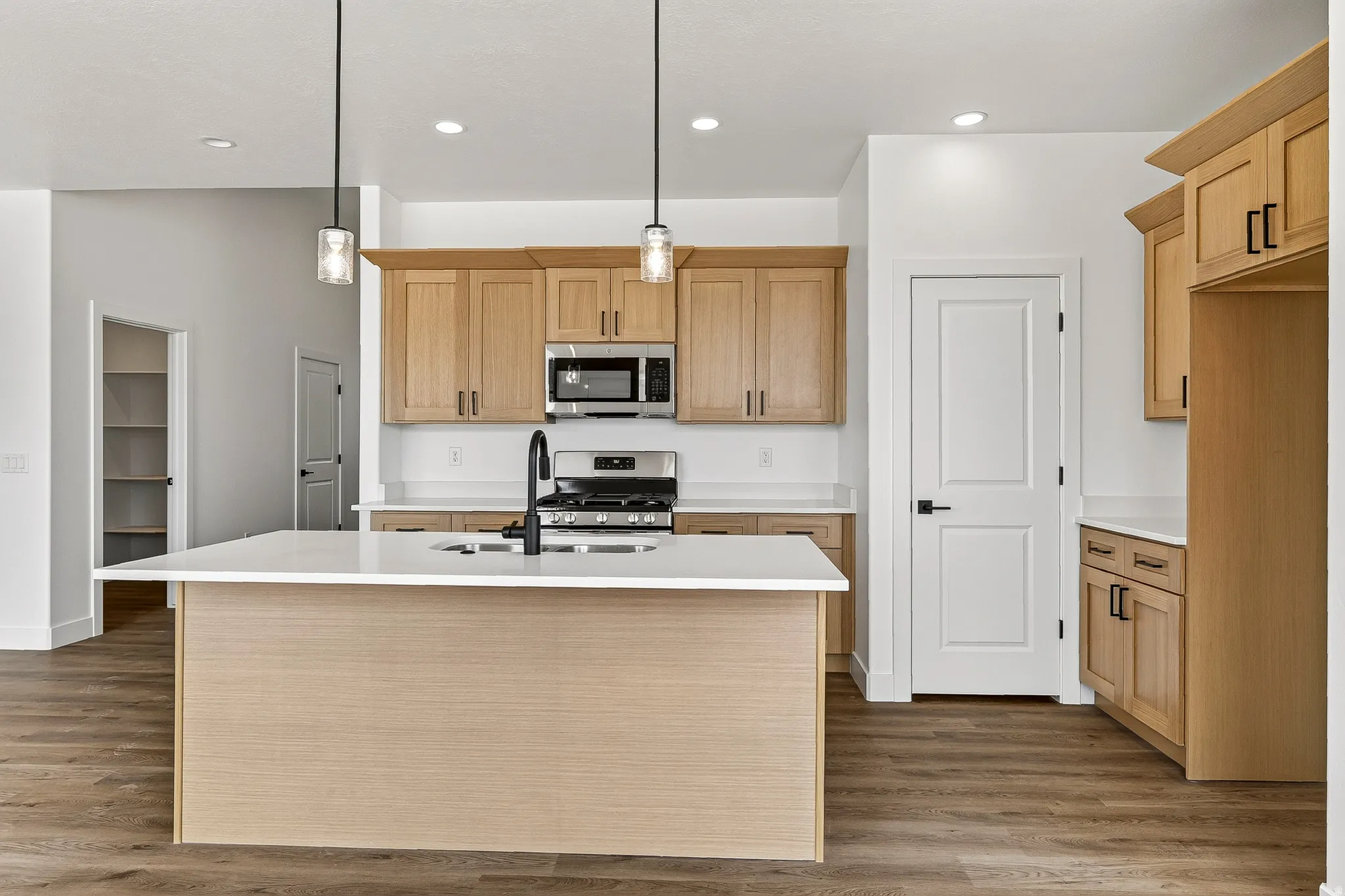 Modern kitchen featuring light wood cabinetry, a central island with a white countertop, and wood-finish flooring