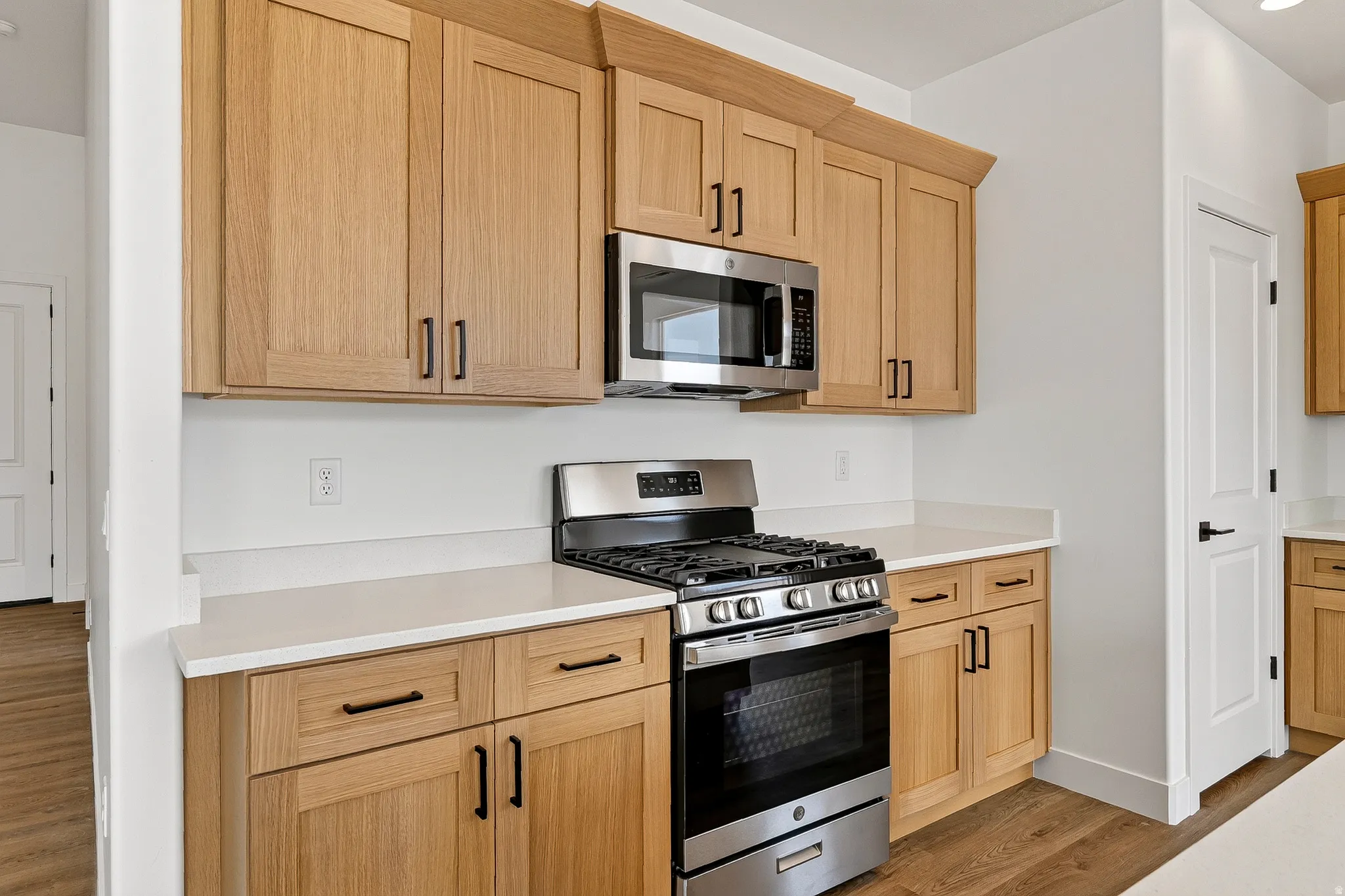 Modern kitchen featuring light wood cabinetry with black hardware, white countertops, stainless steel gas range, and a built-in microwave