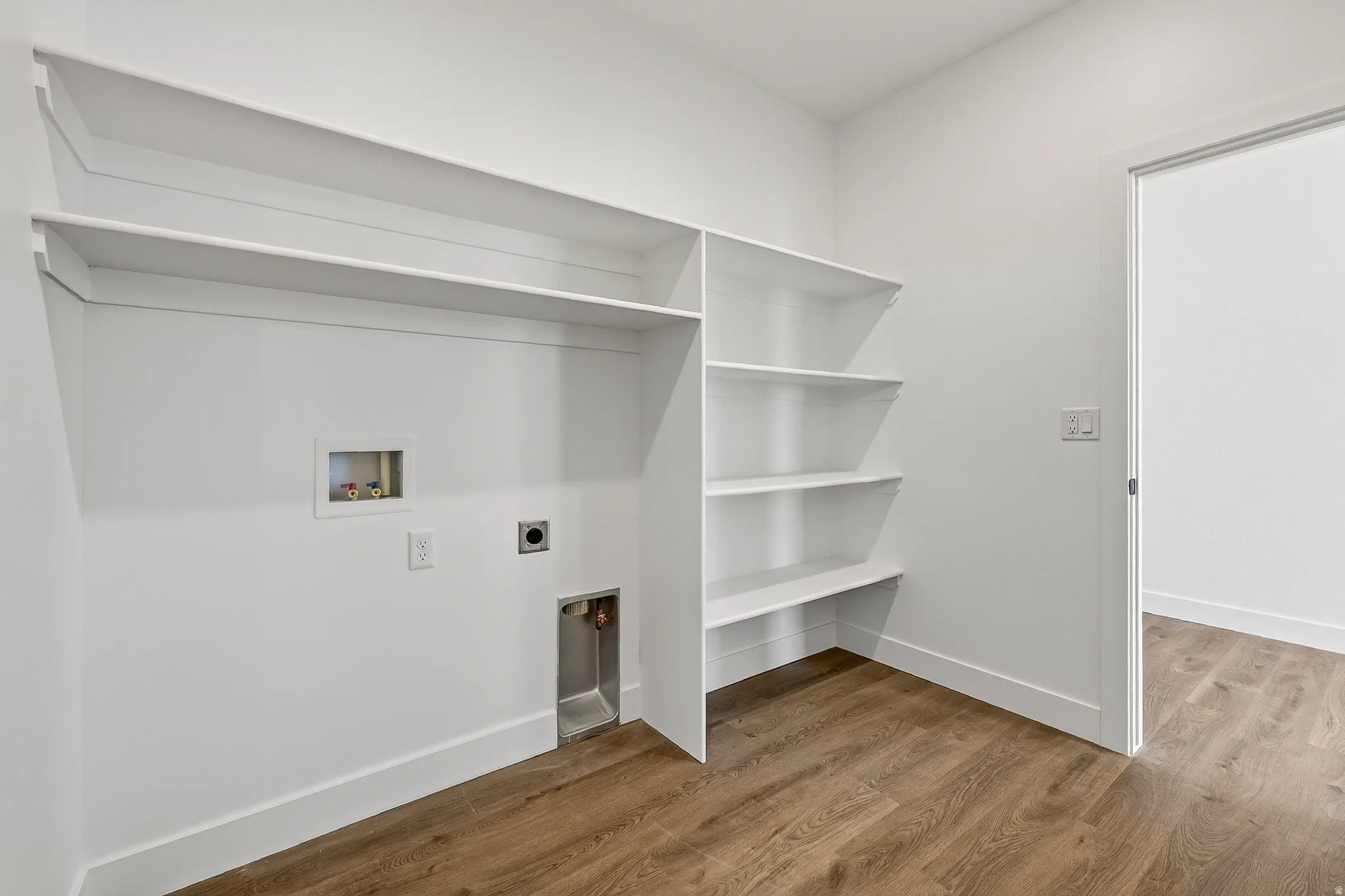 Dedicated laundry area with wood-finish flooring, built-in shelving, and a white baseboard trim