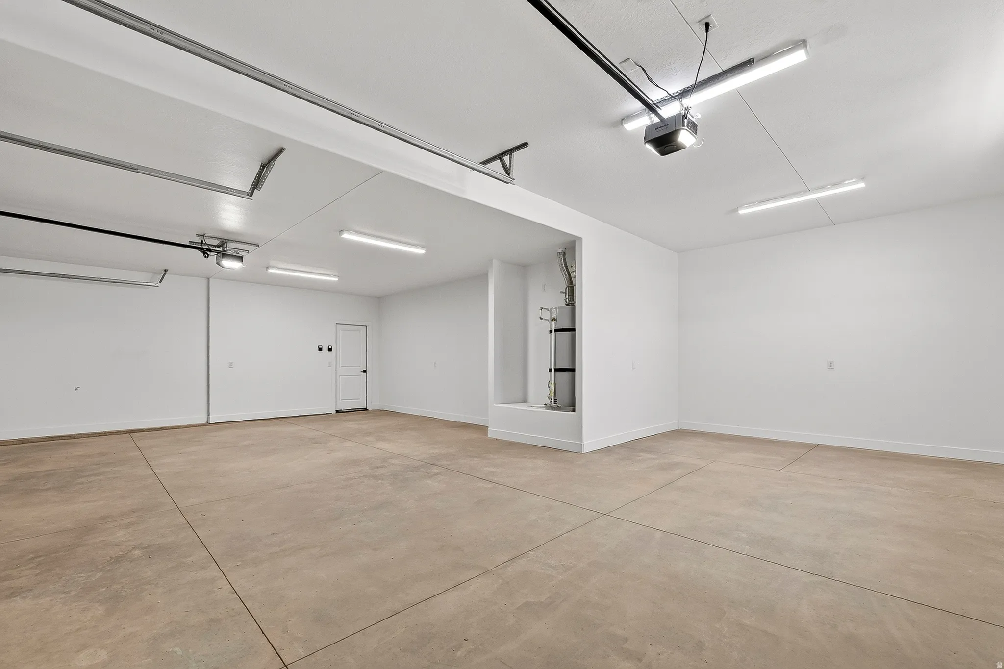 Spacious garage featuring a concrete floor, bright overhead lighting, white painted walls, and a white interior door with black hardware