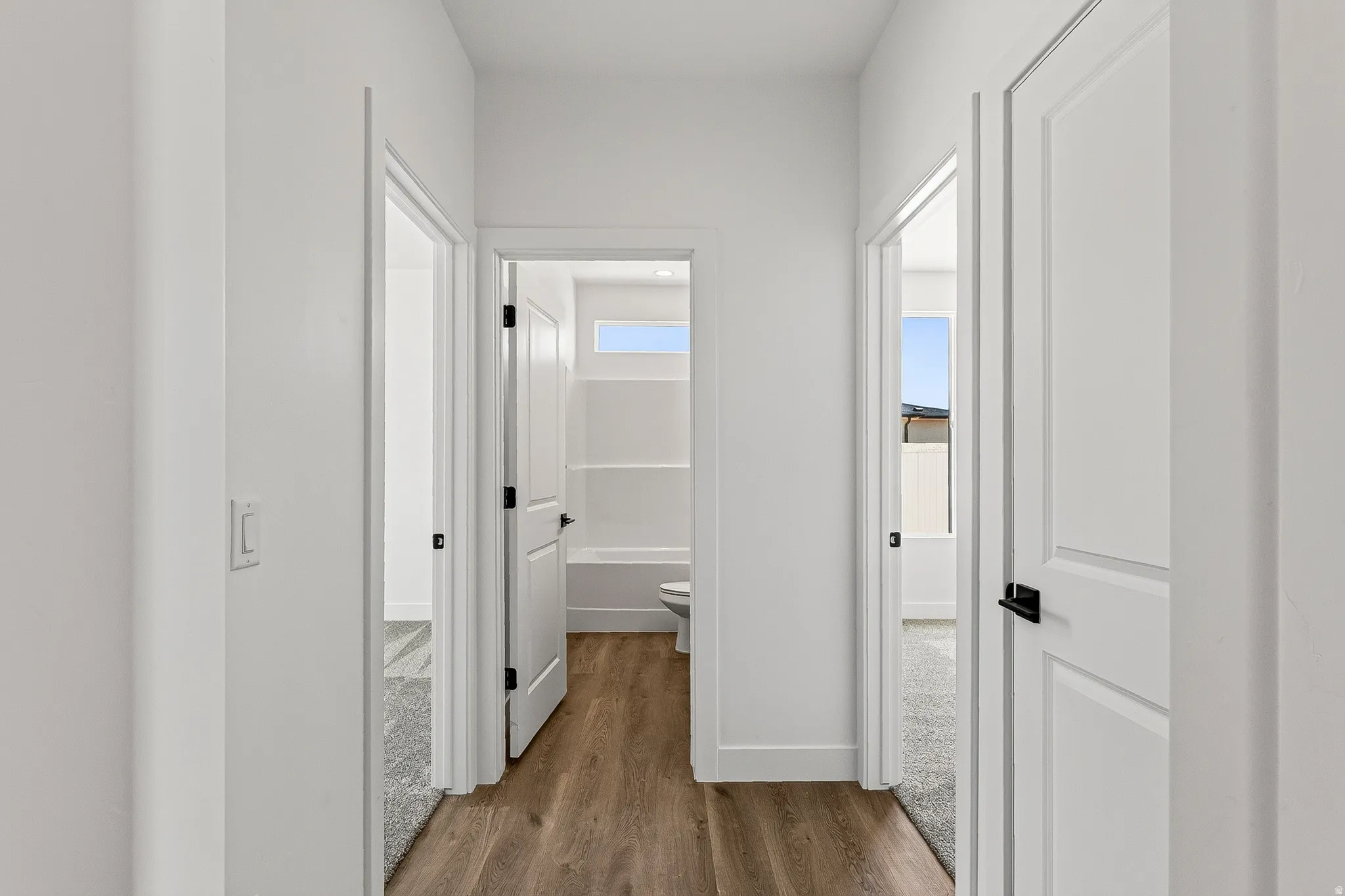 Hallway featuring wood-finish flooring, white paneled doors with matte black hardware, and crisp white walls
