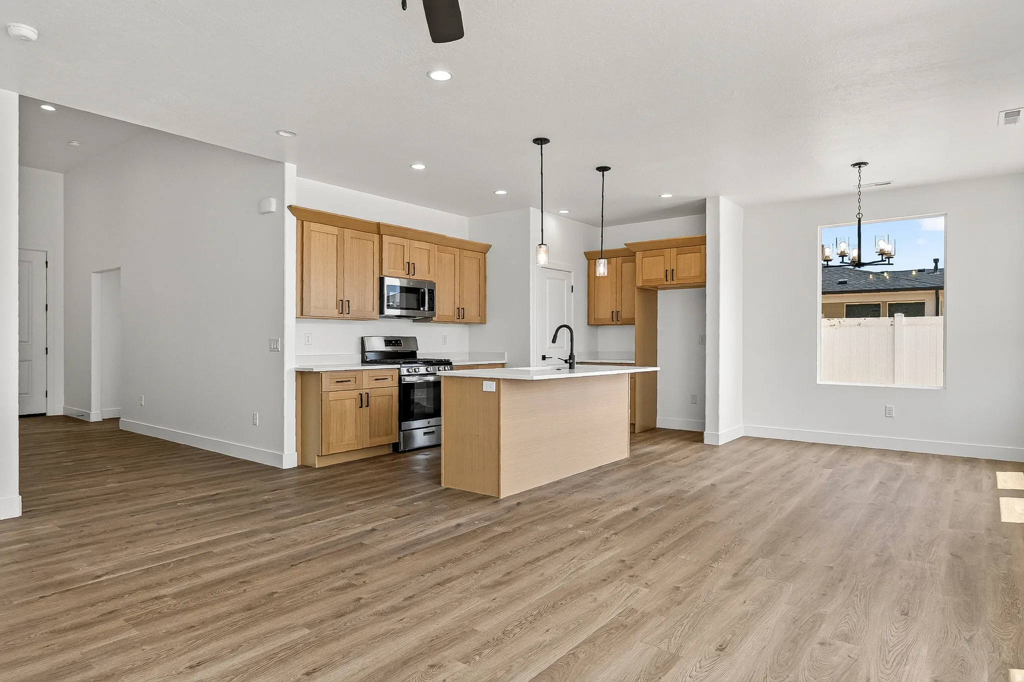 Open-concept kitchen and living area featuring wood-finish flooring, a kitchen island with pendant lighting, stainless steel appliances, light wood cabinetry, and recessed lighting