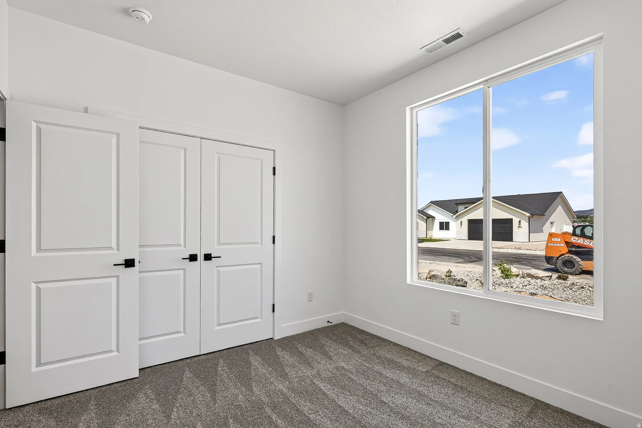 Bright interior space featuring a large window, white walls, and gray patterned carpet