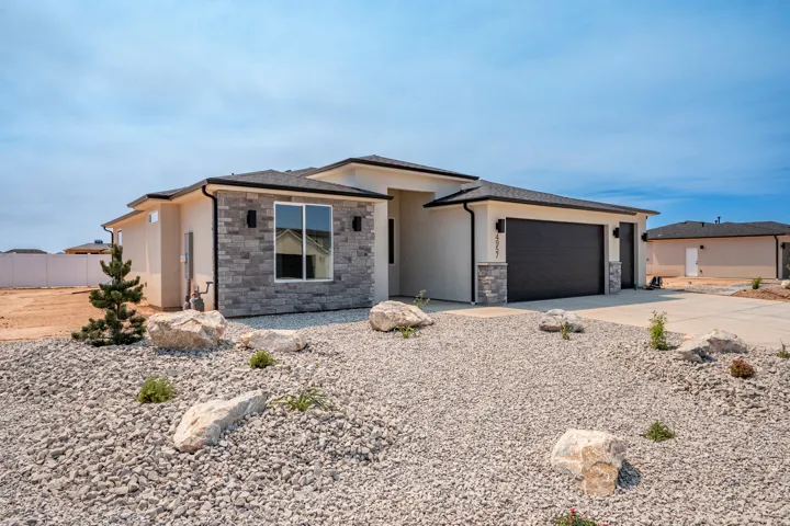Contemporary stucco exterior with stacked stone accents, a dark garage door, and a gravel and boulder landscape