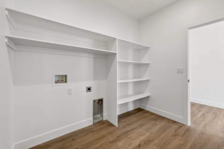 Dedicated laundry area with wood-finish flooring, built-in shelving, and a white baseboard trim