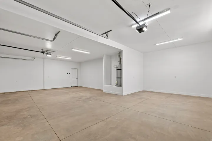 Spacious garage featuring a concrete floor, bright overhead lighting, white painted walls, and a white interior door with black hardware