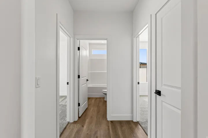 Hallway featuring wood-finish flooring, white paneled doors with matte black hardware, and crisp white walls