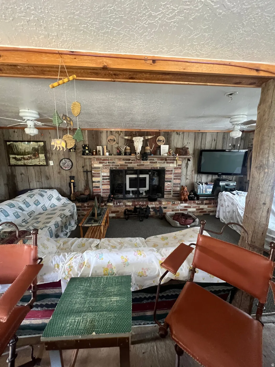 Living area with wooden and masonry walls, a textured ceiling, a fireplace, and ceiling fan
