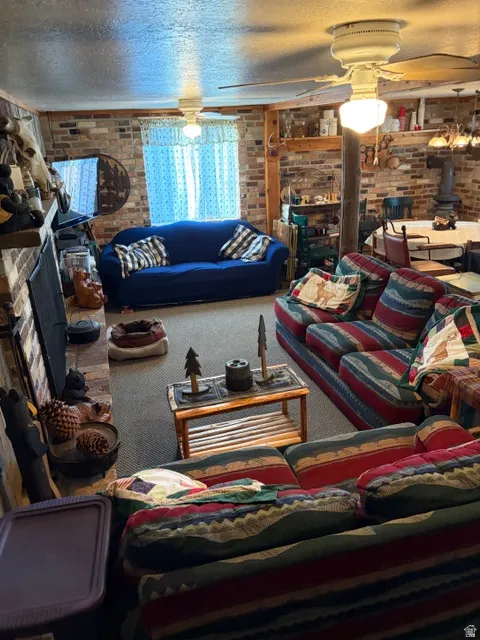 Carpeted living area featuring a wood stove, brick wall, a ceiling fan, a textured ceiling, and a fireplace