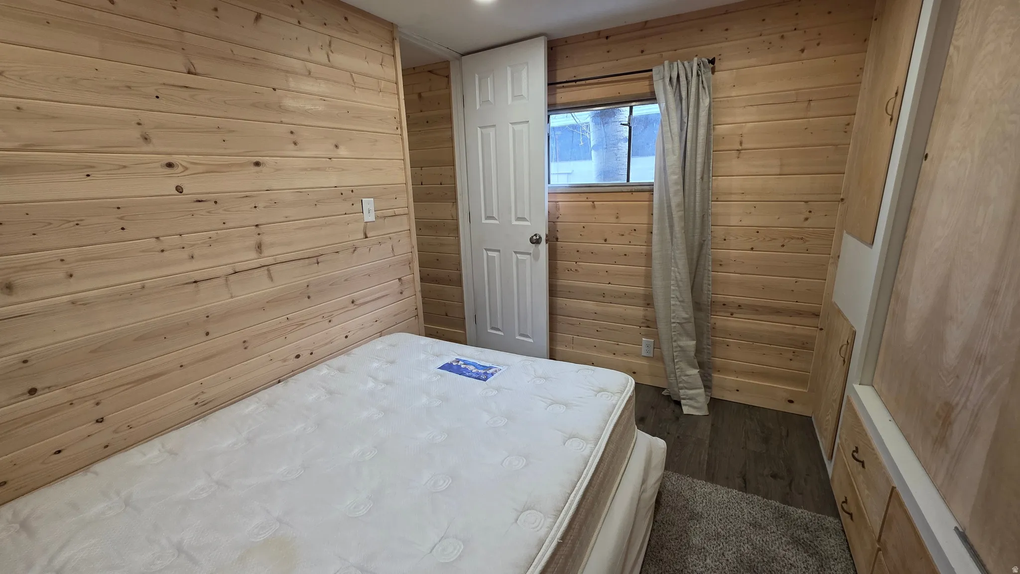 Bedroom with wooden walls and dark wood-style floors