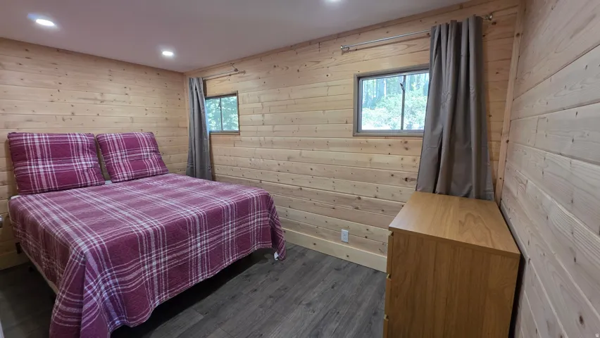 Recessed lighting illuminates a room featuring natural wood plank walls, two windows, and wood-finish flooring