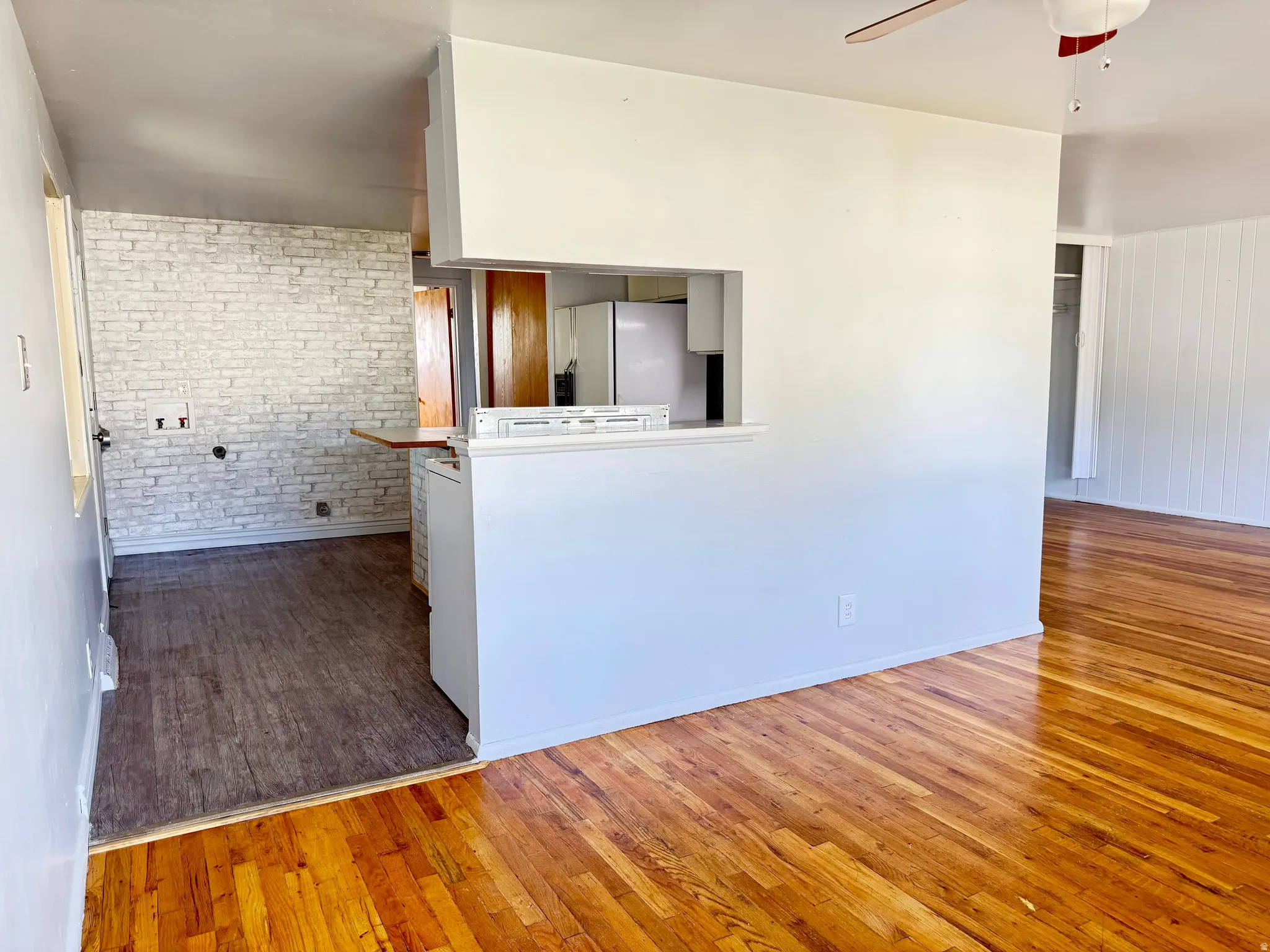 Kitchen featuring wood-type flooring, stainless steel refrigerator with ice dispenser, a ceiling fan, and brick wall