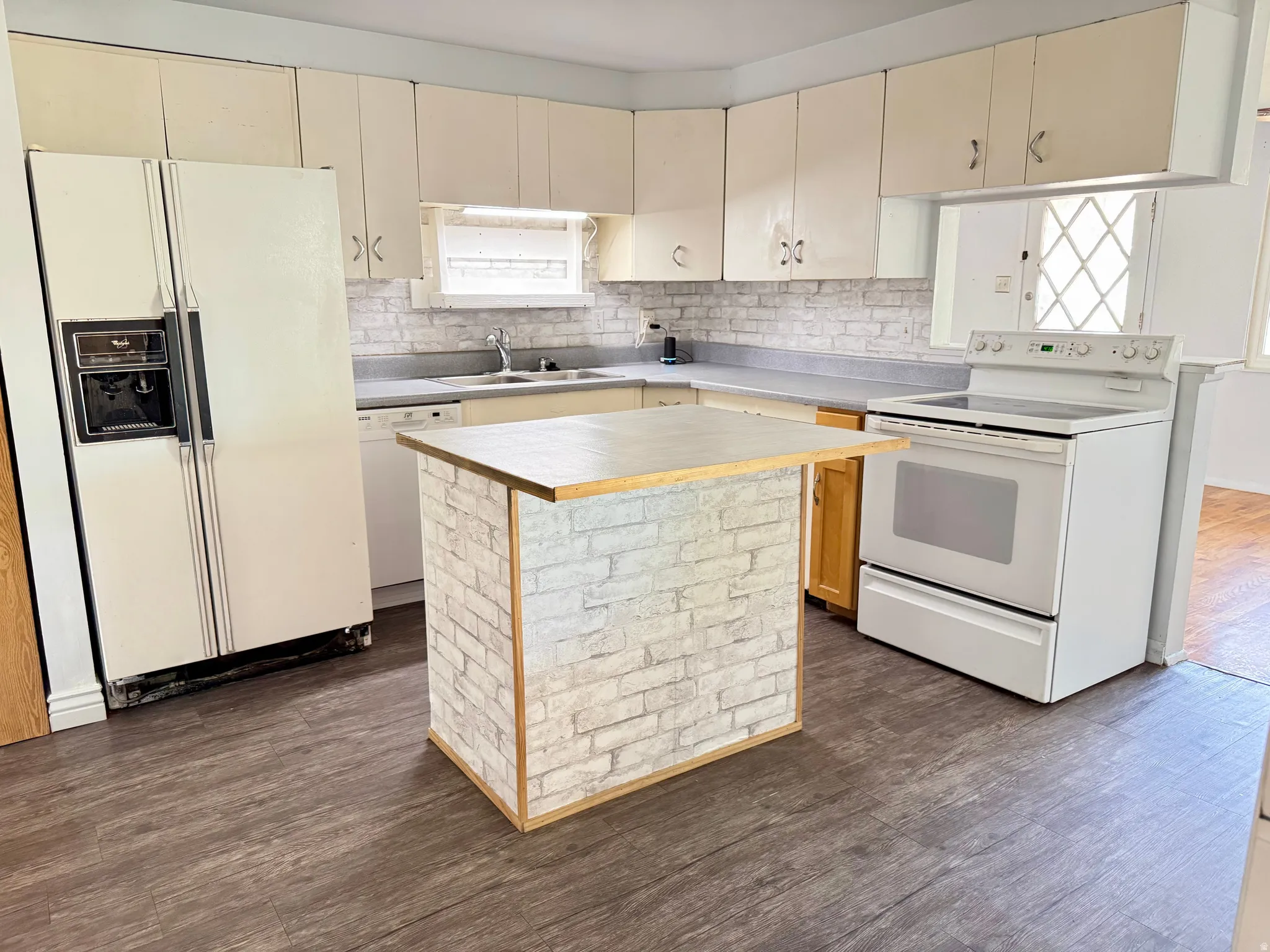 Kitchen with white appliances, dark wood-type flooring, a kitchen island, cream cabinets, and tasteful backsplash
