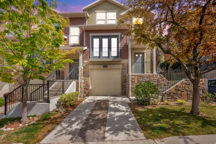 Traditional home featuring concrete driveway, an attached garage, stone siding, and a balcony