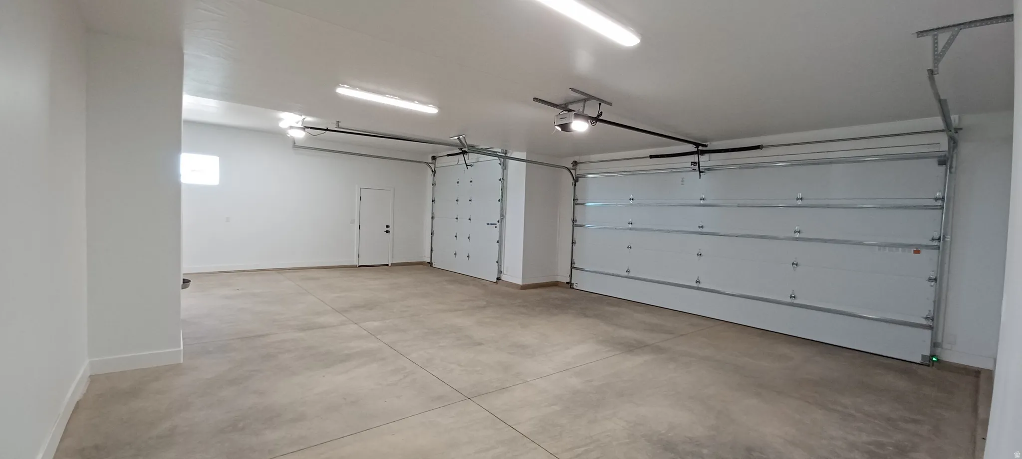 Spacious garage featuring a light concrete floor, multiple overhead garage doors, an internal access door, a small window, and bright overhead strip lighting
