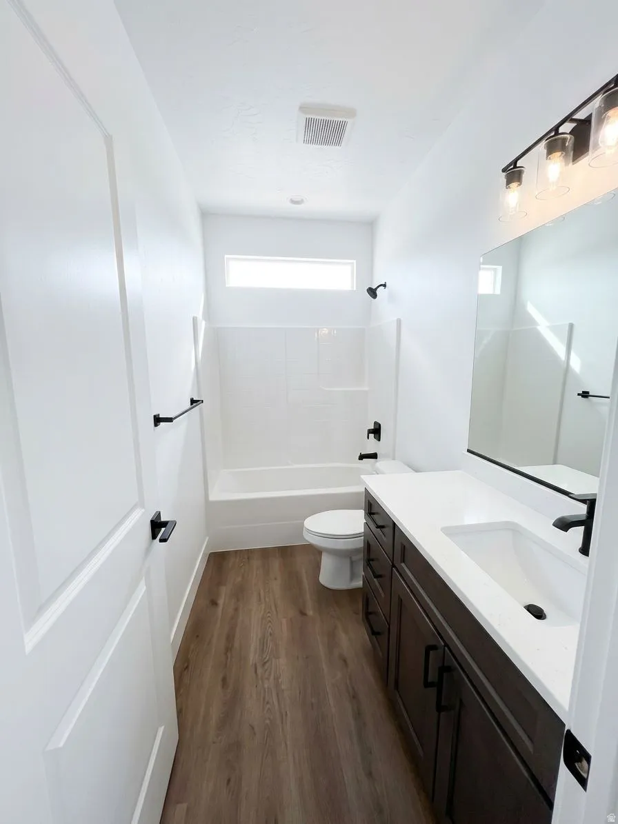 Contemporary bathroom featuring a wood-finish floor, dark wood-finish vanity with ample storage, white countertop, and a white tub/shower combination