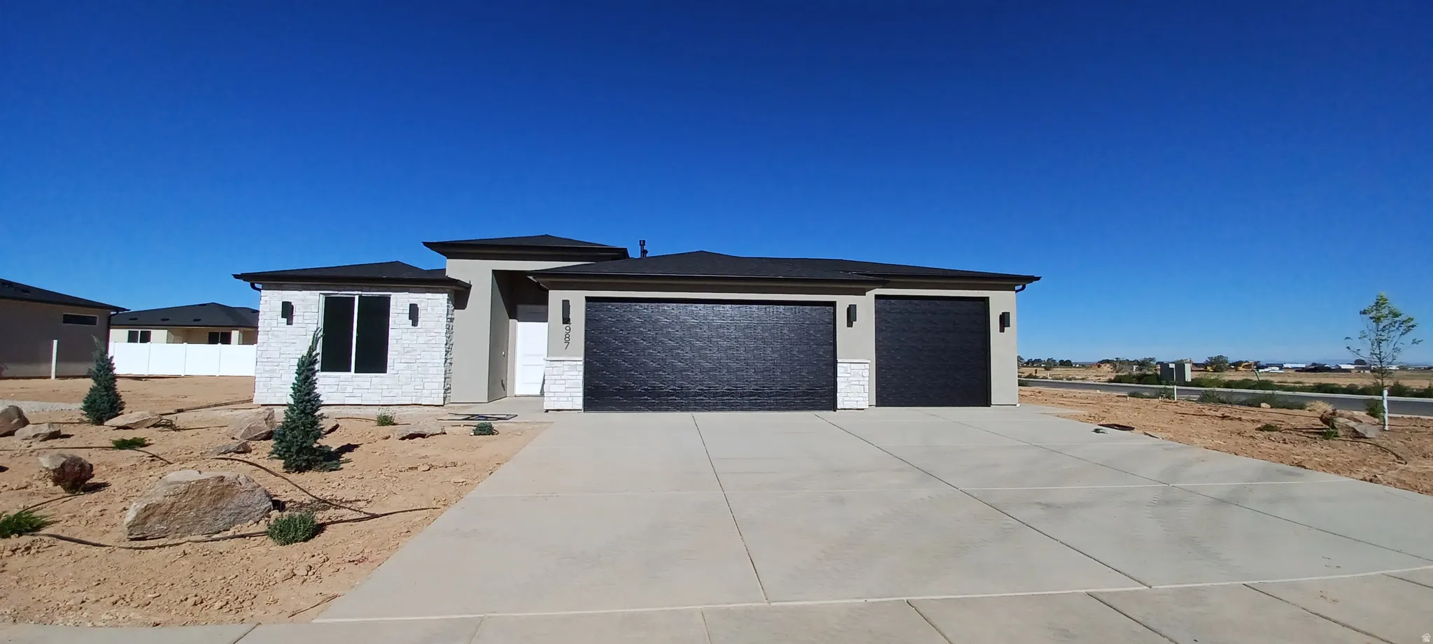 Contemporary exterior featuring light stucco and stacked stone accents, a dark shingle roof, and a concrete driveway leading to two dark garage doors