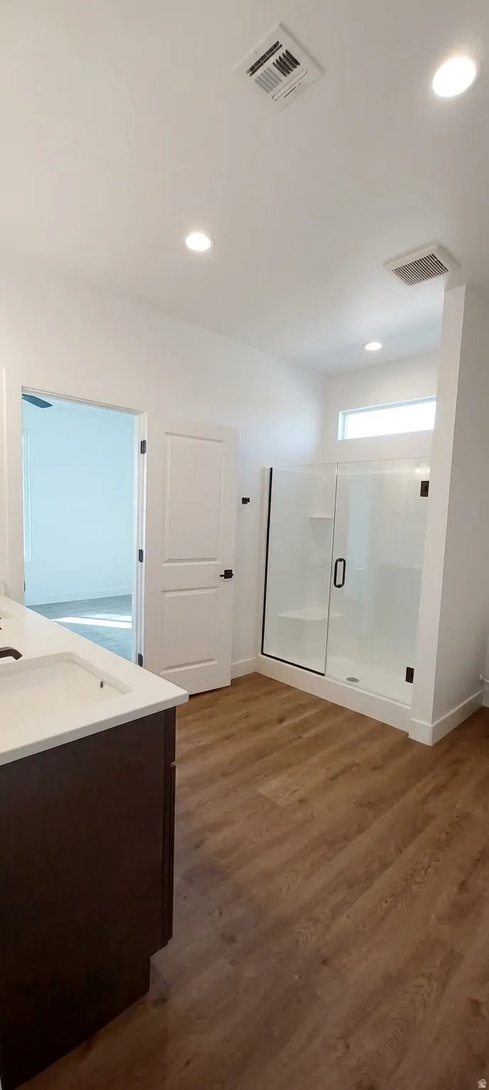 Wood-finish flooring, white walls, and recessed ceiling lighting complement the dark wood-finish vanity with a white countertop and rectangular sink