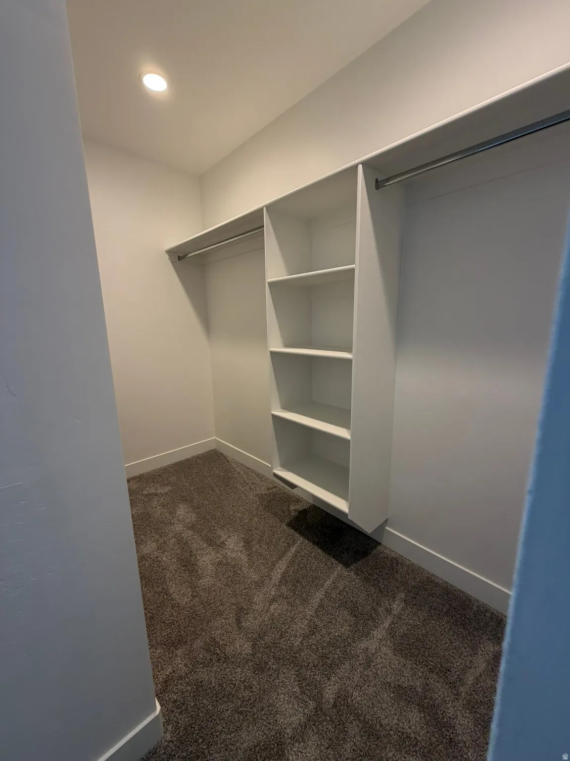 Recessed ceiling lighting, built-in shelving, dual hanging rods, and gray carpet flooring