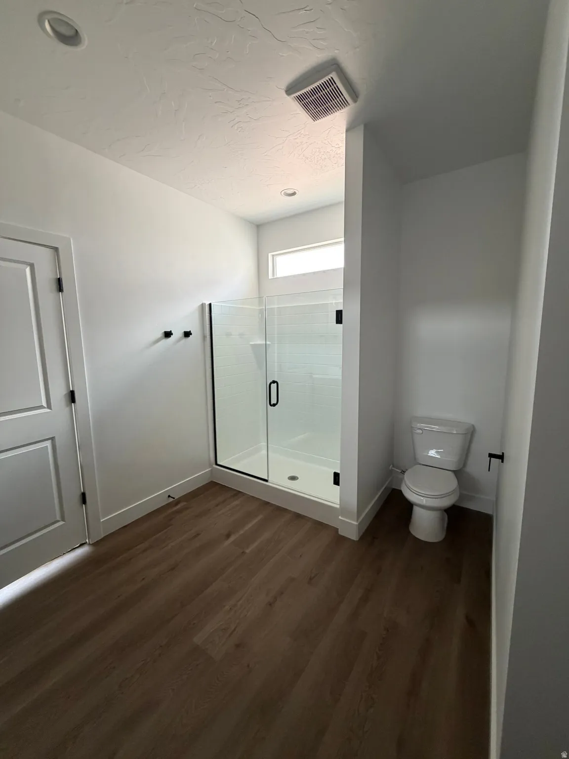 Glass-enclosed shower with a white tiled surround, wood-finish flooring, and a white toilet