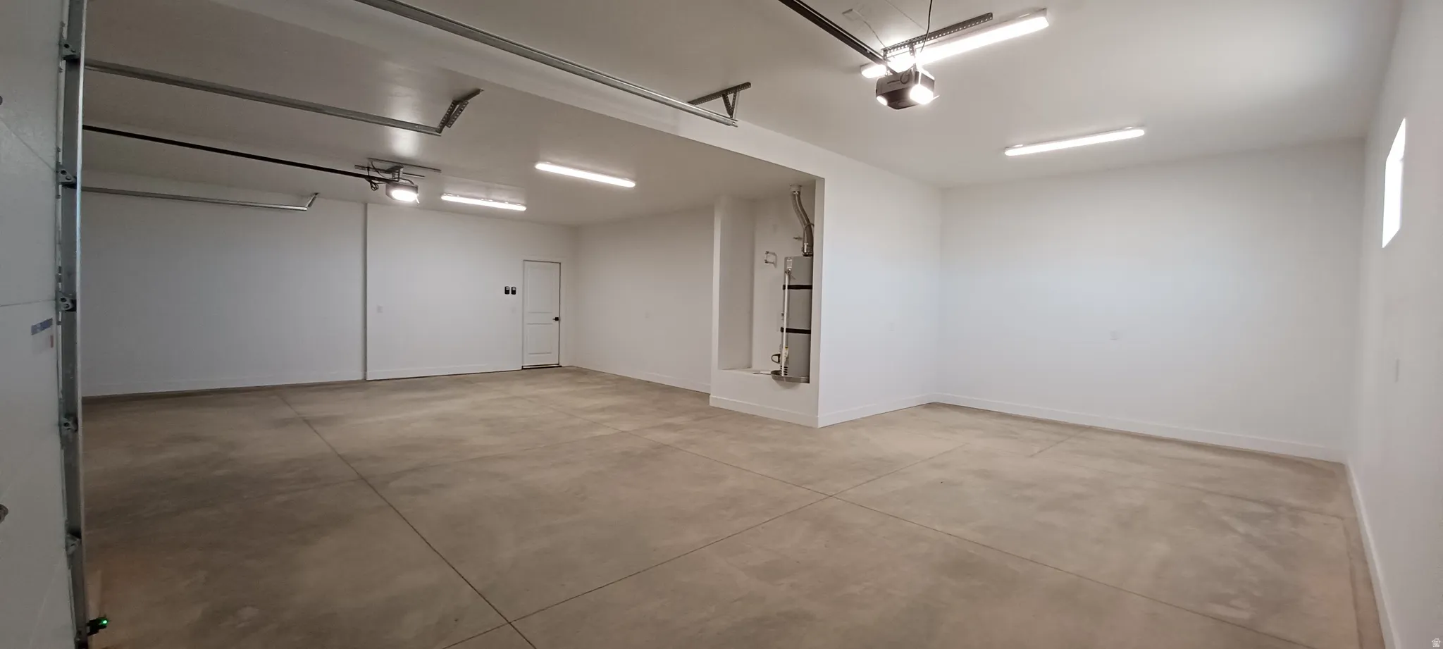 Spacious garage featuring a concrete floor, multiple fluorescent light fixtures, and a garage door opener system