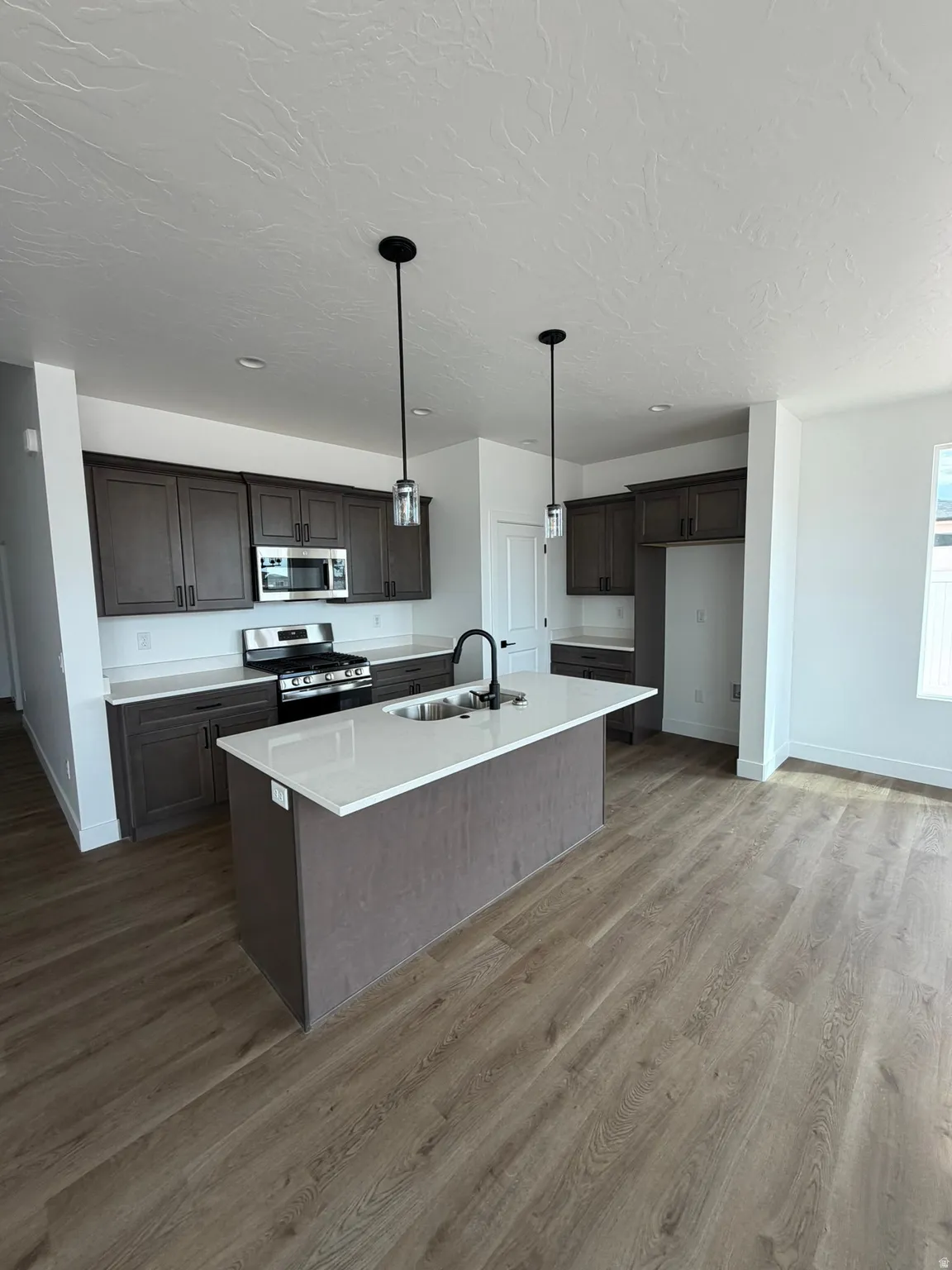 Open-concept kitchen featuring an island with a white countertop, dark wood-finish cabinetry, stainless steel appliances, and pendant lighting