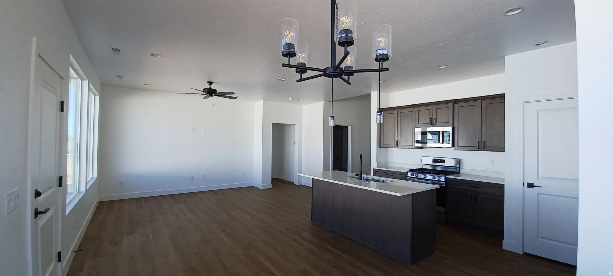 Open-concept living area with wood-finish flooring, a contemporary chandelier, and a ceiling fan