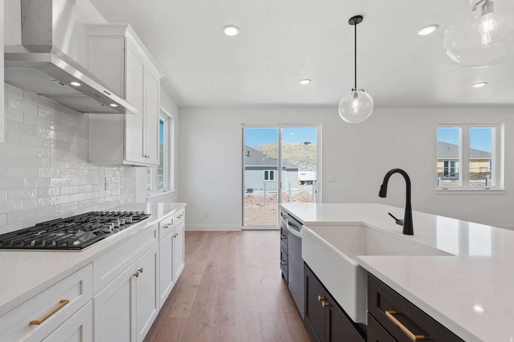 Kitchen with two tone color scheme, light stone countertops, light wood finished floors, stainless steel appliances, and decorative light fixtures