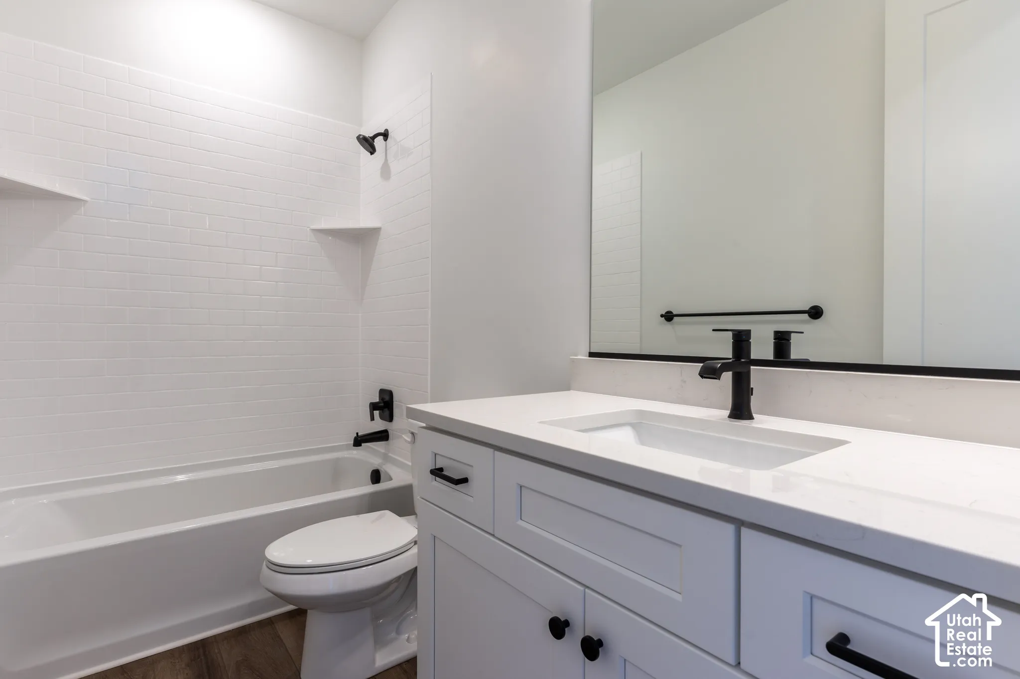 Bathroom featuring a white subway tile surround, white vanity with shaker-style cabinetry, matte black fixtures, integrated sink, and wood-finish flooring