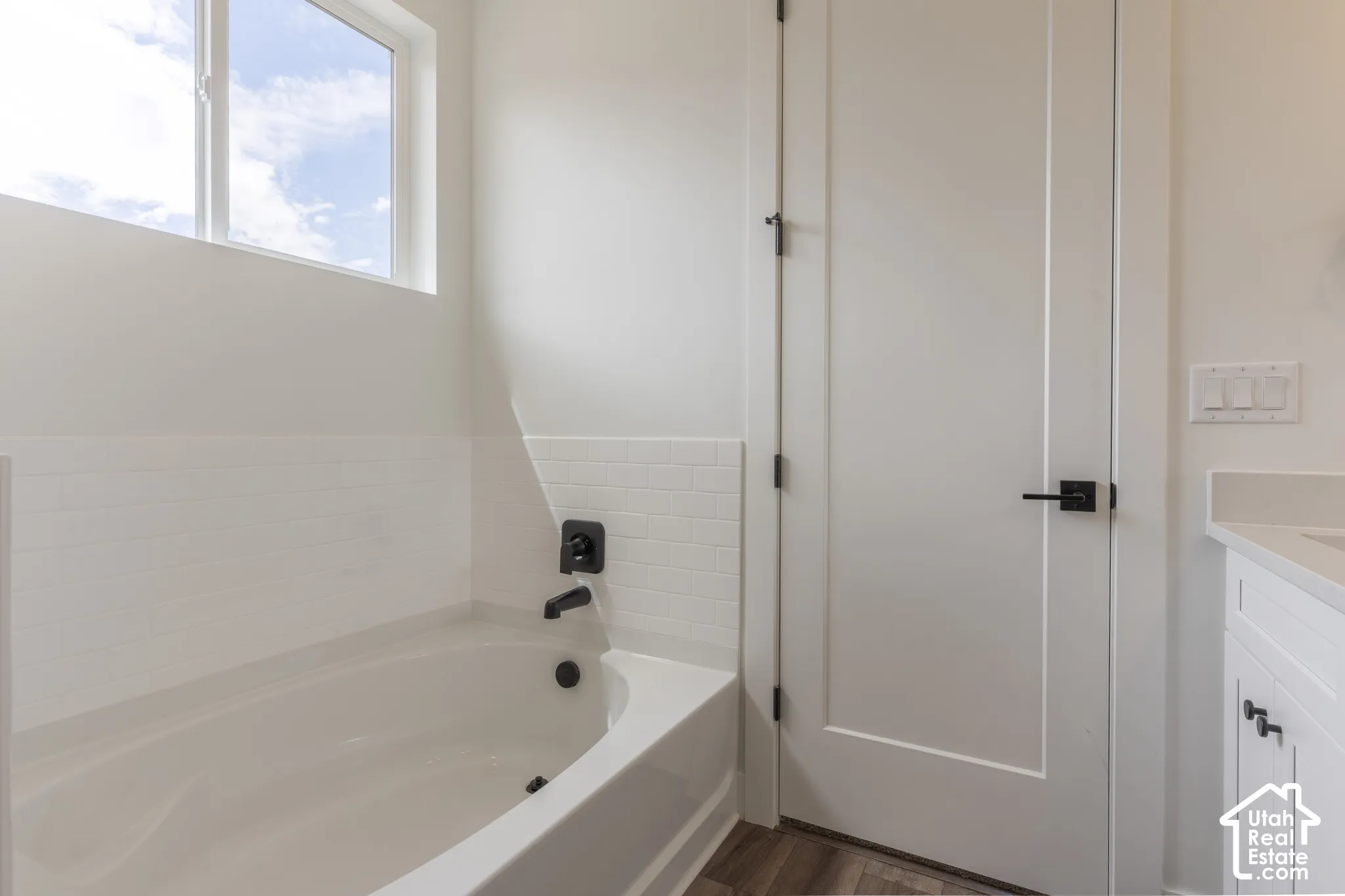 White bathtub with matte black fixtures, white subway tile surround, and high transom window