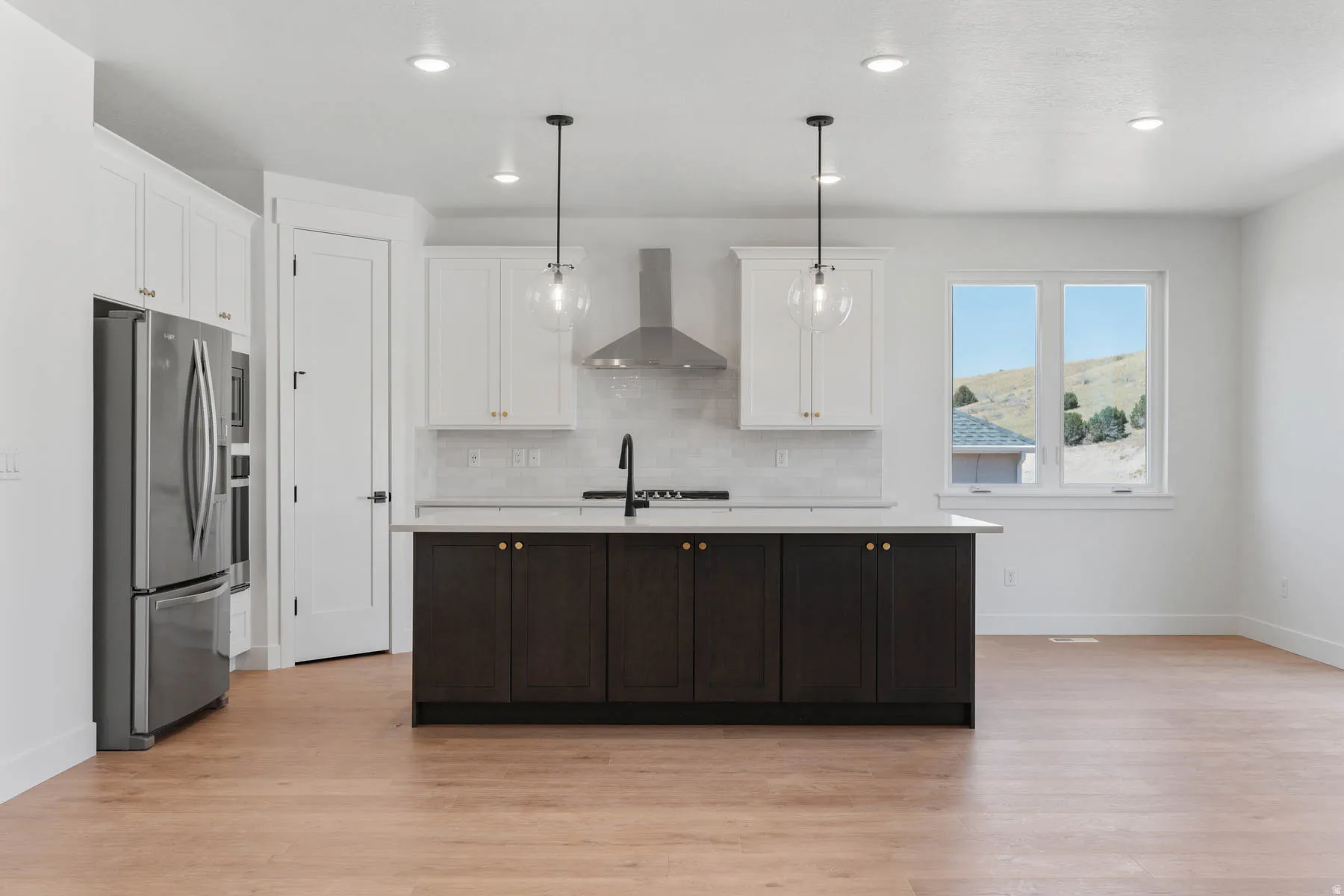 Kitchen featuring stainless steel fridge with ice dispenser, an island with sink, pendant lighting, light wood-style flooring, and dual tone cabinetry