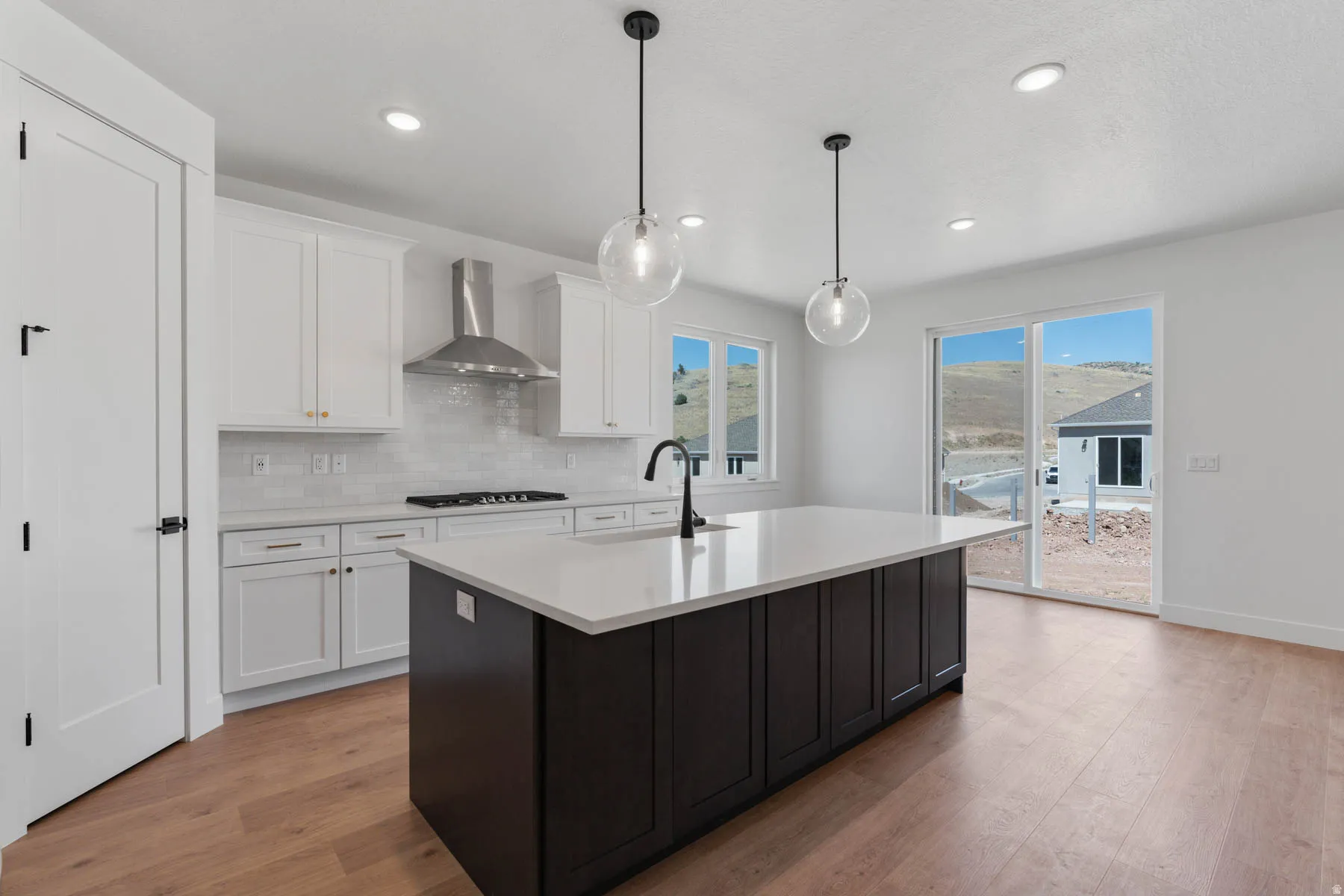 Dual tone kitchen featuring dual tone cabinetry, light wood-style flooring, pendant lighting, a center island with sink, and tasteful backsplash