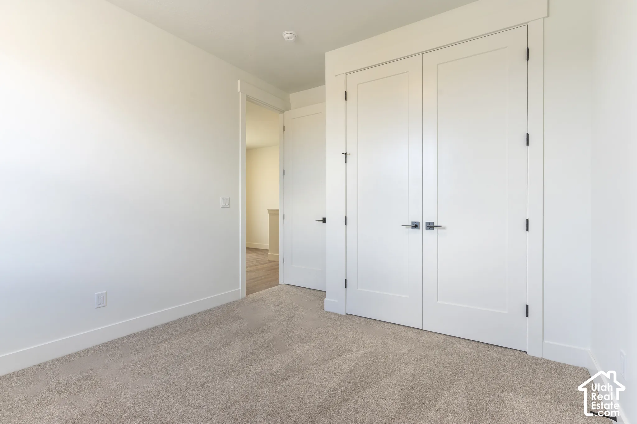 Neutral tone carpet flooring, white walls, white double doors with brushed nickel hardware, and thick white baseboards