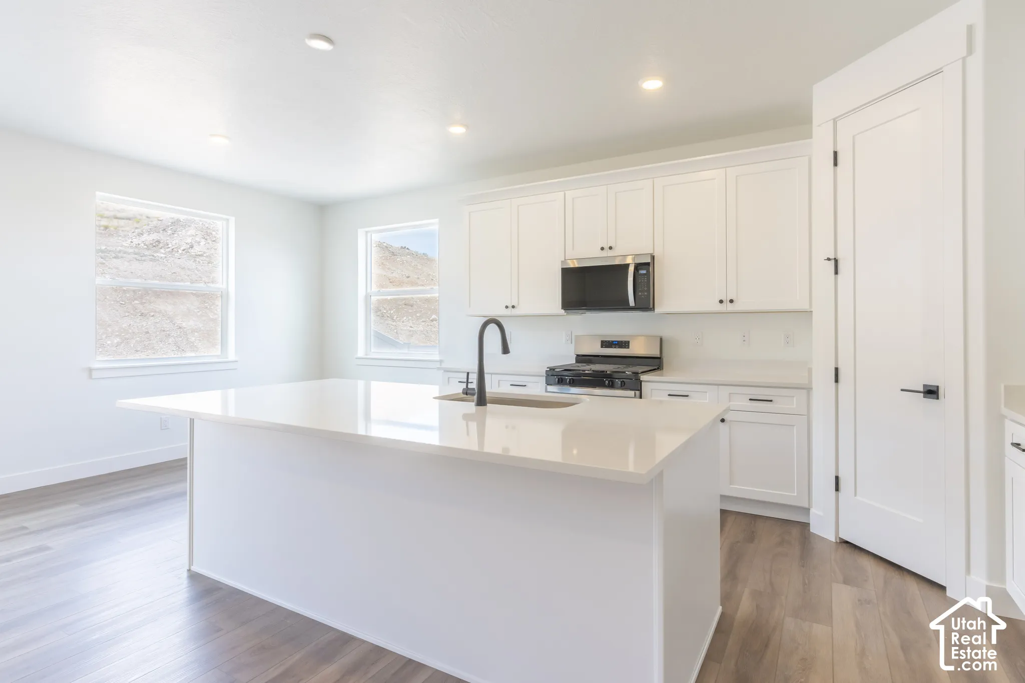 Kitchen featuring a large island with a light-toned countertop, white cabinetry with dark hardware, stainless steel appliances, and wood-finish flooring