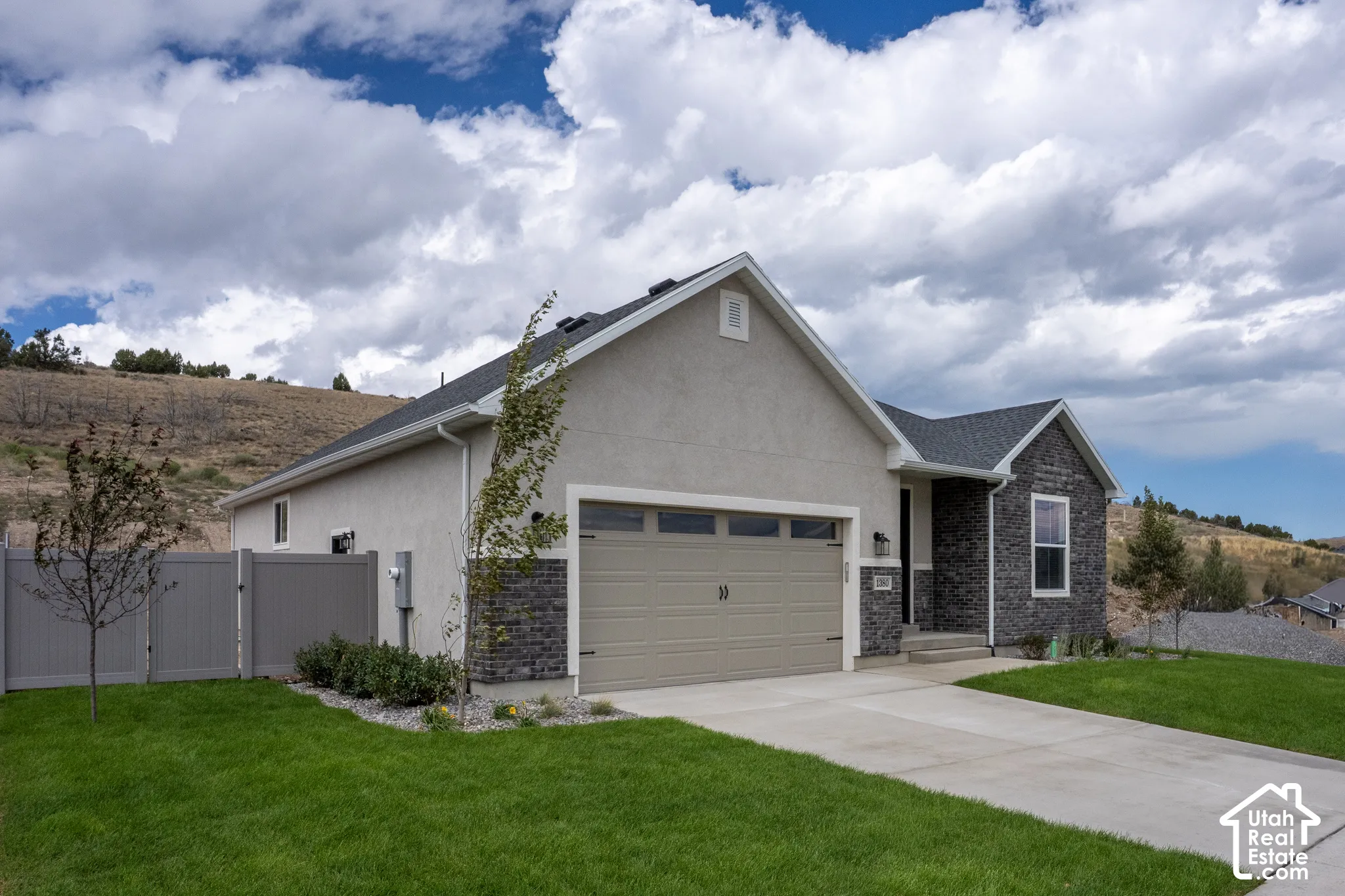 Stucco and stone facade with an attached two-car garage, concrete driveway, and a fenced yard