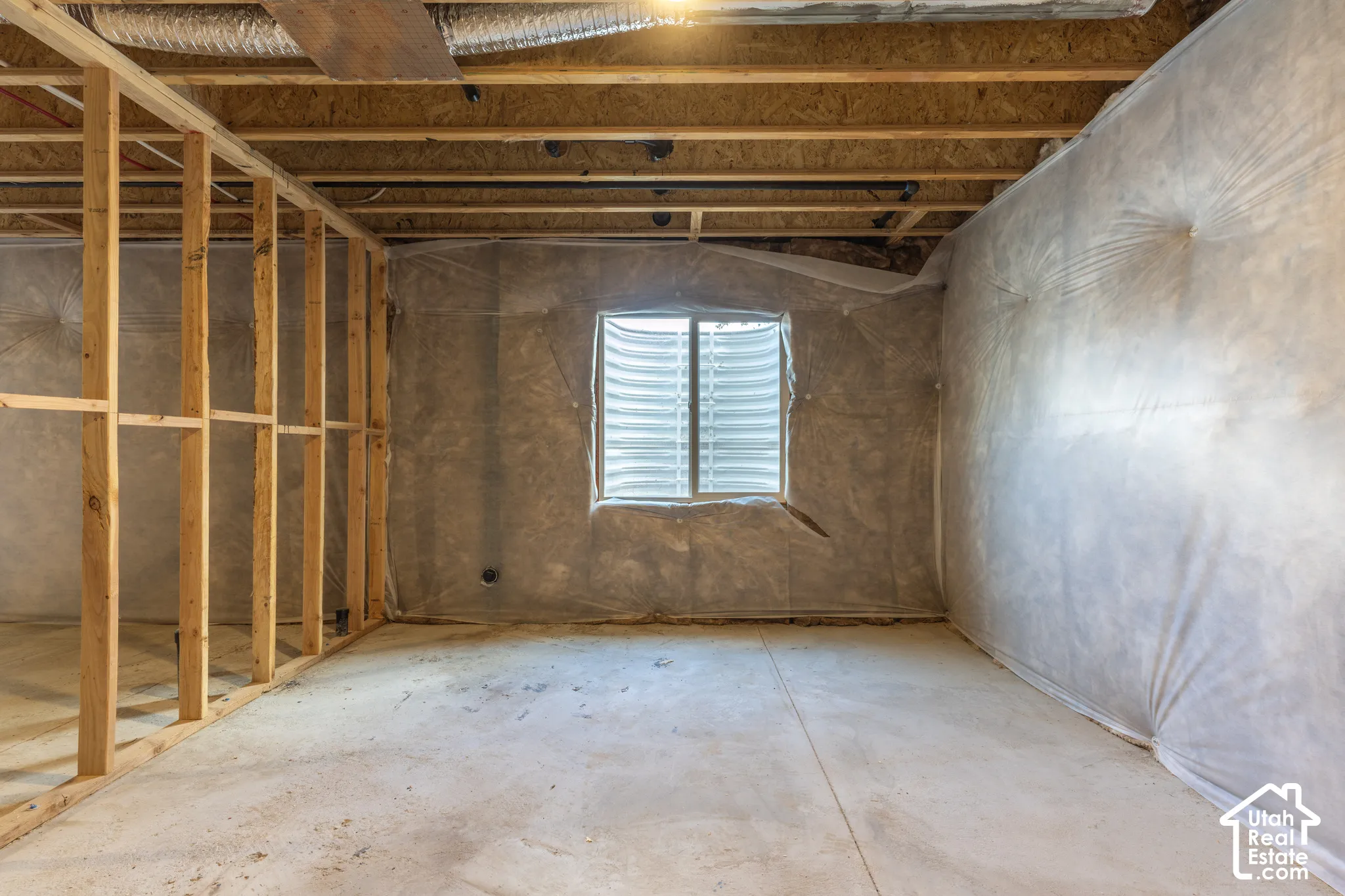 Unfinished basement space featuring exposed wood framing, concrete flooring, a window well, and insulated walls