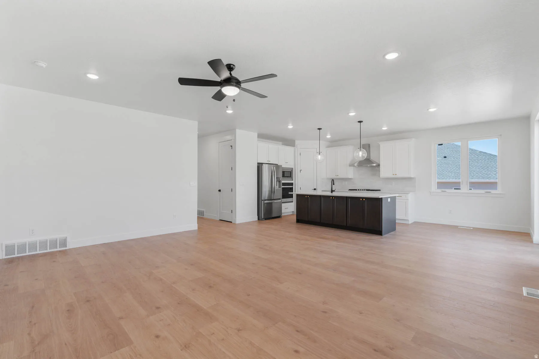 Two tone kitchen with open floor plan, a kitchen island with sink, light countertops, pendant lighting, and dual tone cabinets