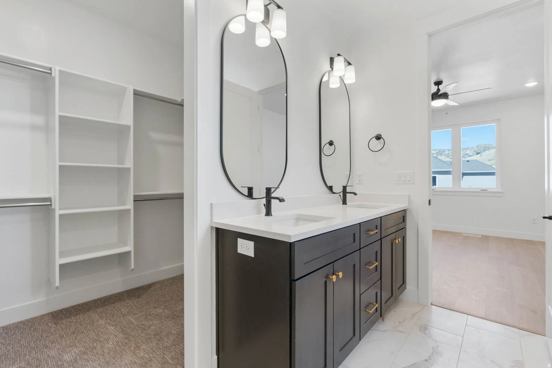 Bathroom featuring a spacious closet, double vanity, a ceiling fan, and light marble finish flooring