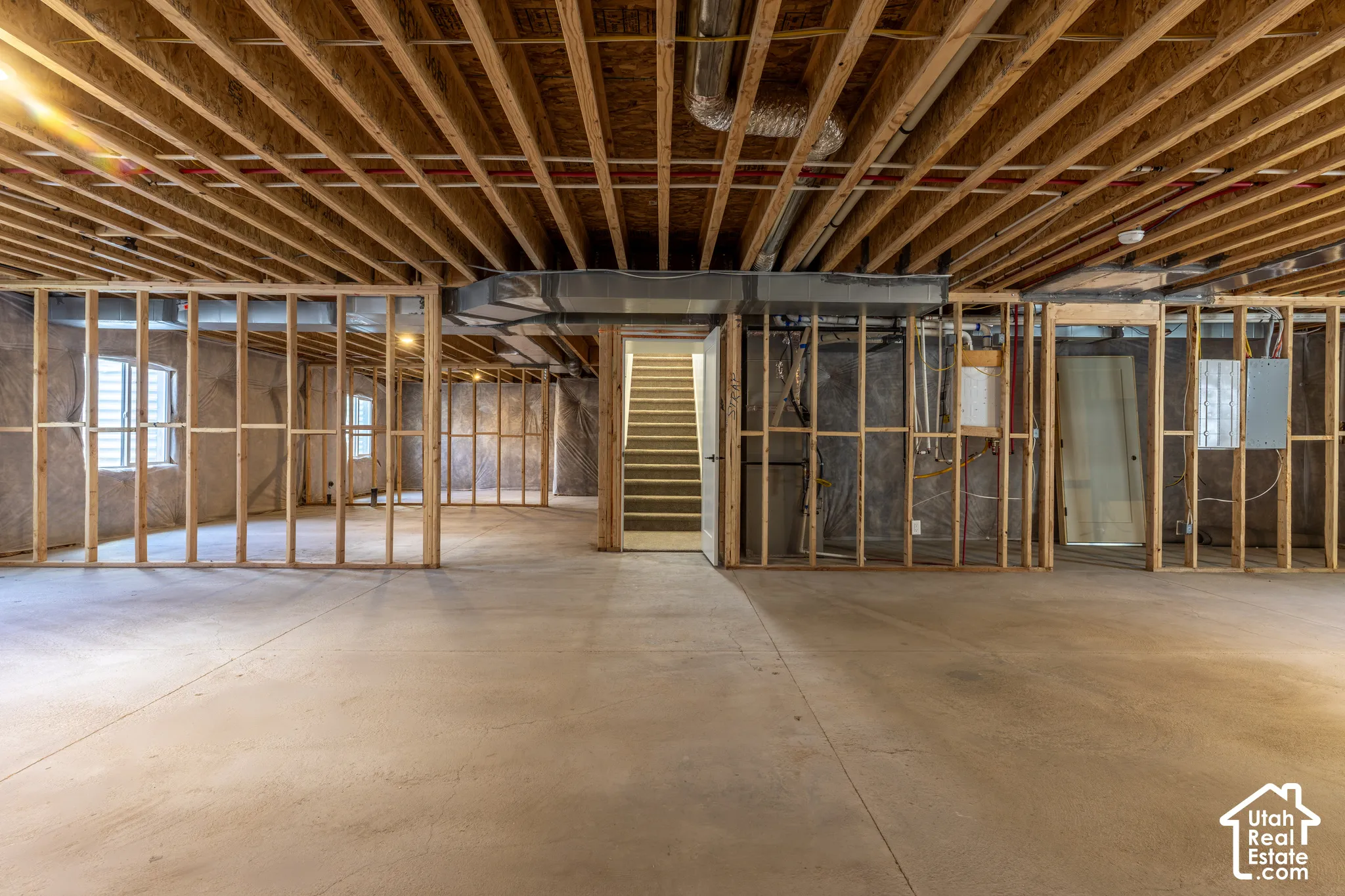 Unfinished basement featuring extensive framing, concrete flooring, exposed ceiling joists, and multiple windows