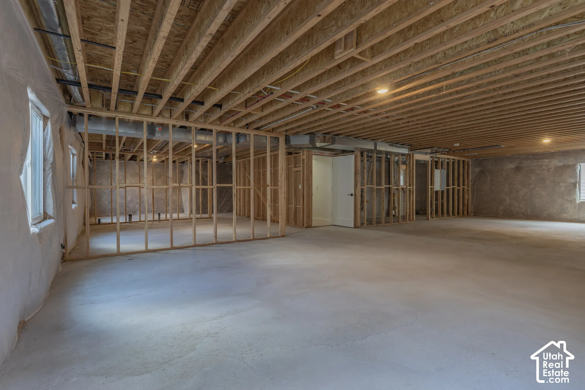 Unfinished basement with exposed ceiling joists, framed interior walls, concrete flooring, and multiple windows