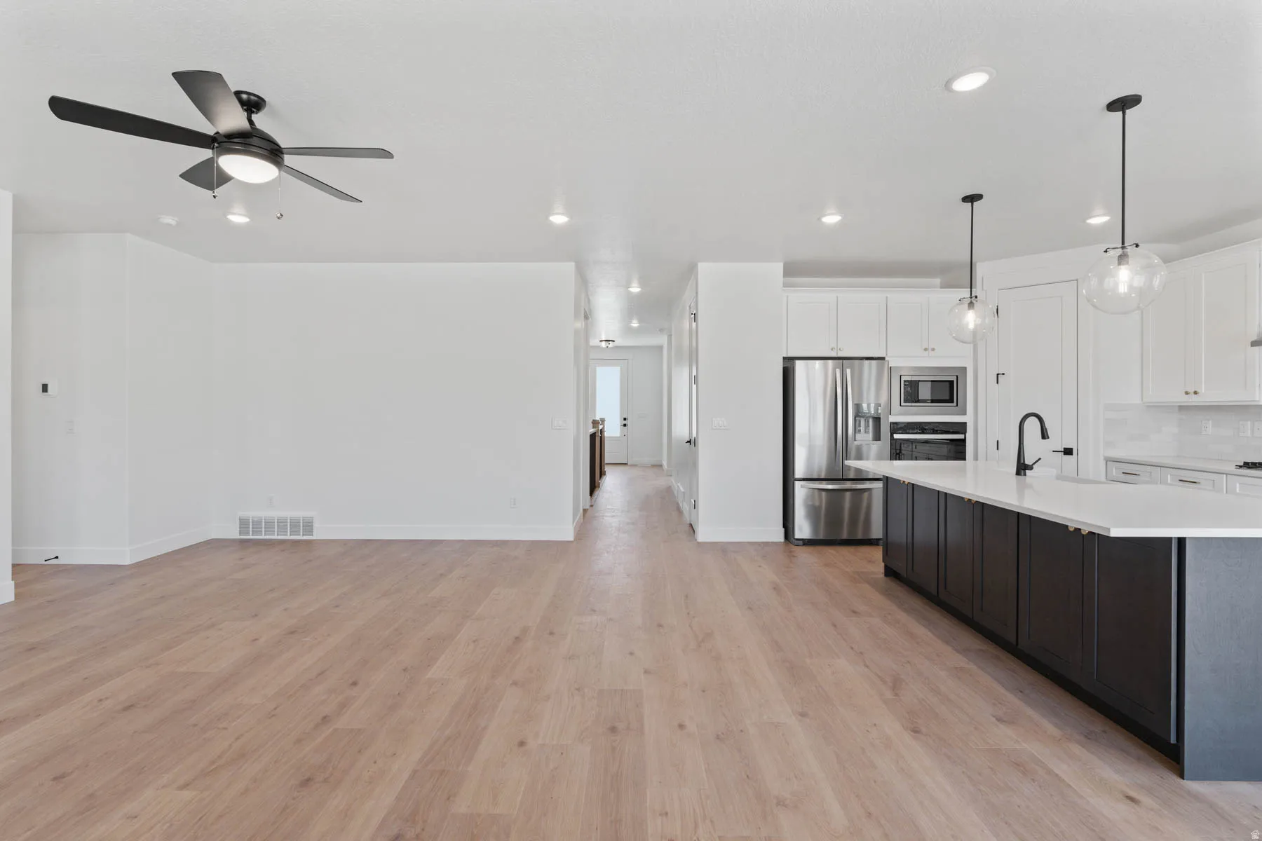 Kitchen with stainless steel appliances, pendant lighting, dual tone cabinets, light wood-style flooring, and a center island with sink