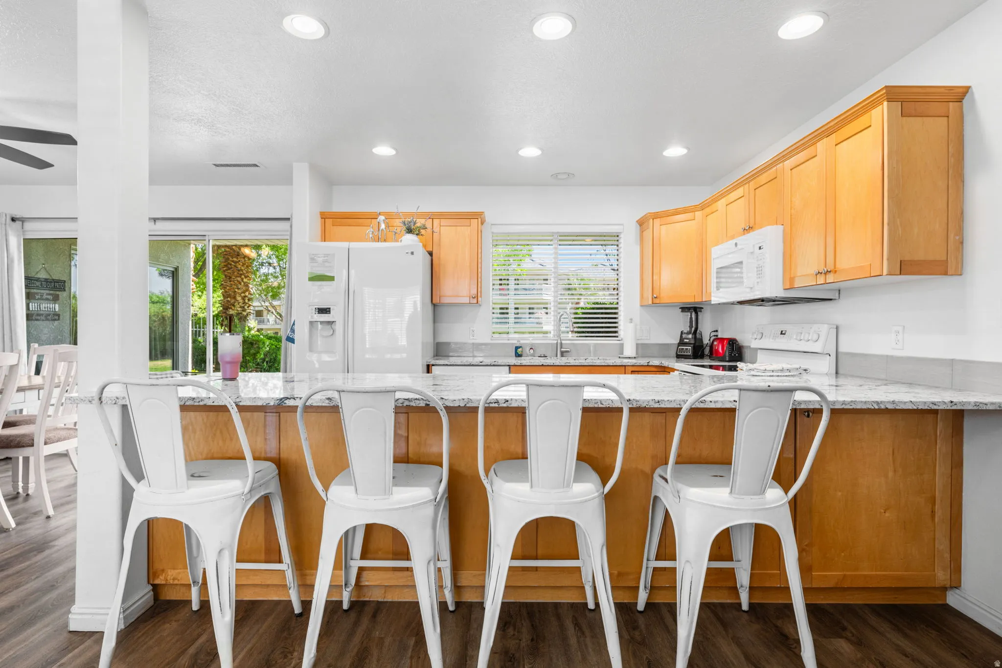 Kitchen featuring a peninsula, light stone countertops, white appliances, a breakfast bar, and dark wood-style floors