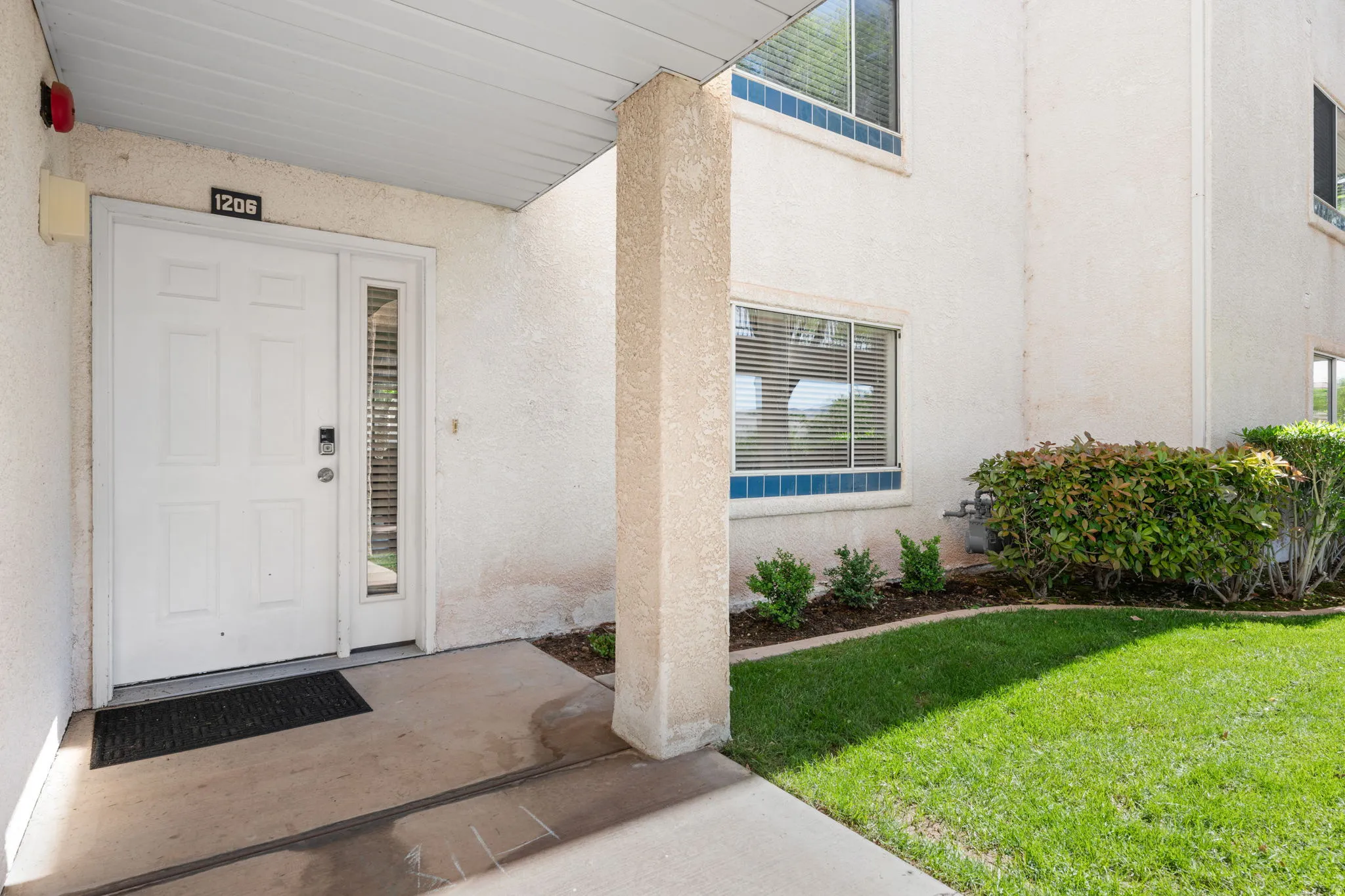 View of exterior entry with a yard, stucco siding, and covered porch