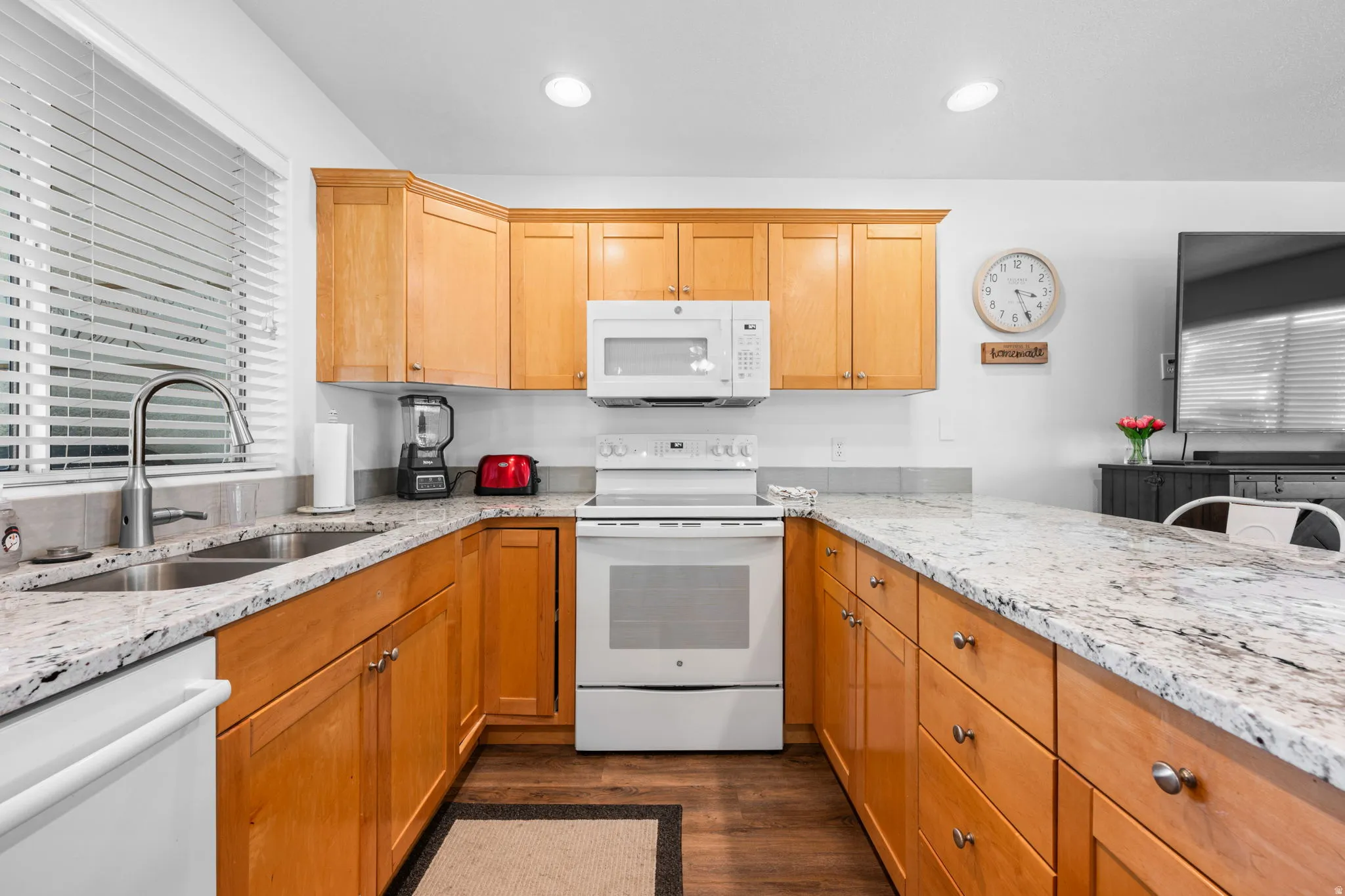 Kitchen with white appliances, light stone countertops, dark wood-style flooring, and recessed lighting