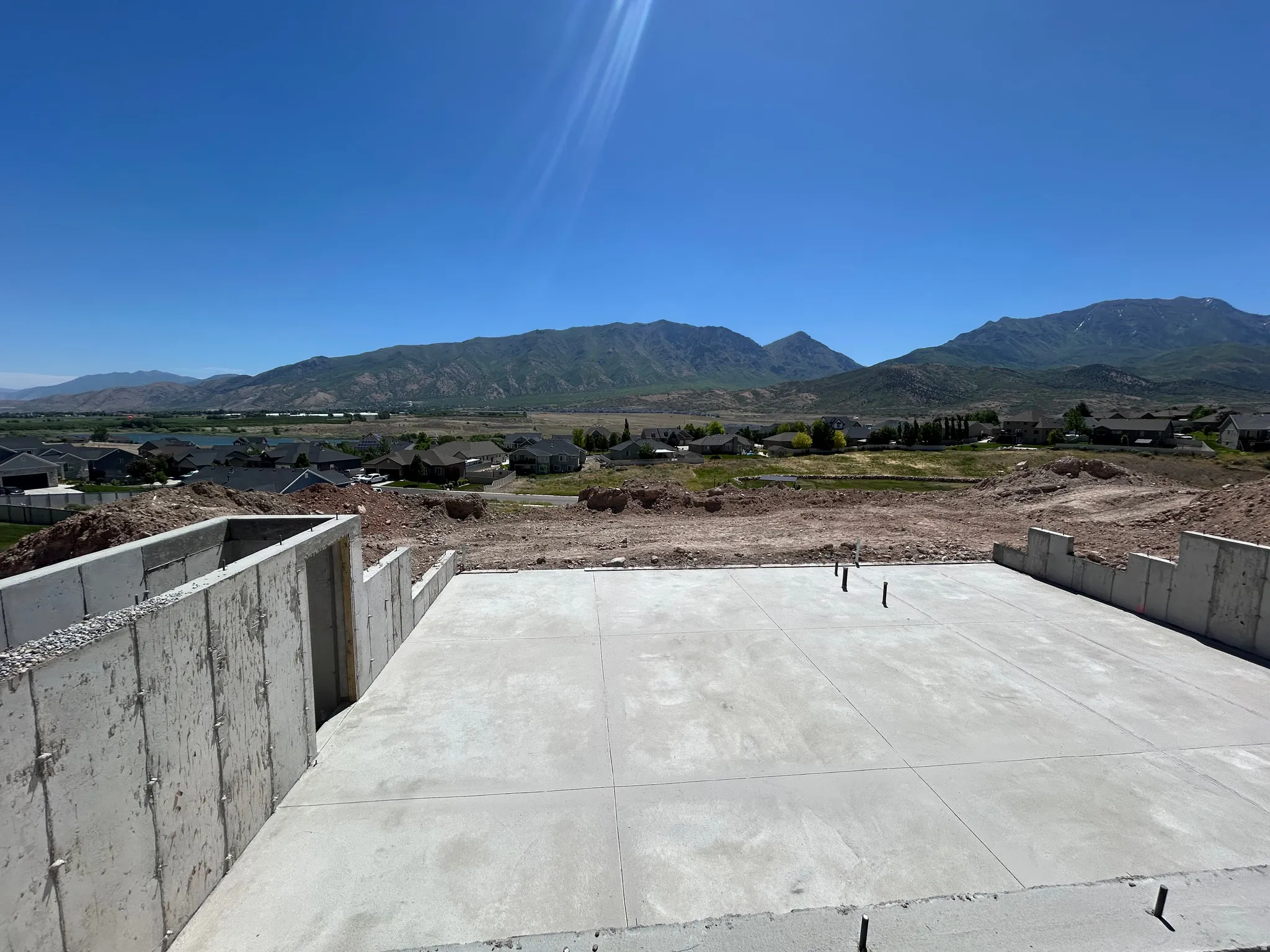 Concrete foundation and basement walls with a mountain backdrop, surrounded by established residential areas and undeveloped terrain